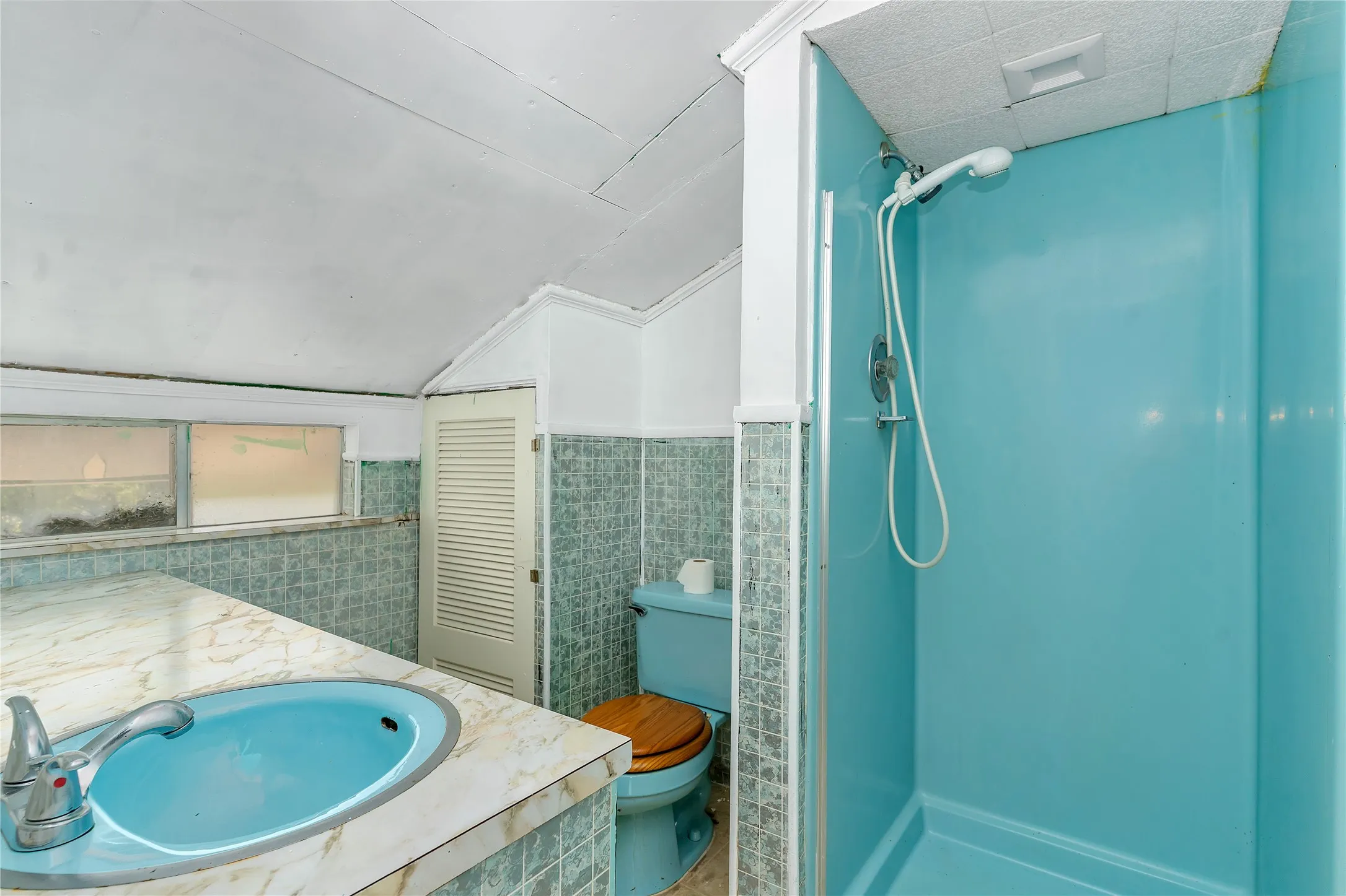 Bathroom featuring double vanity, a stall shower, lofted ceiling, tile walls, and wainscoting