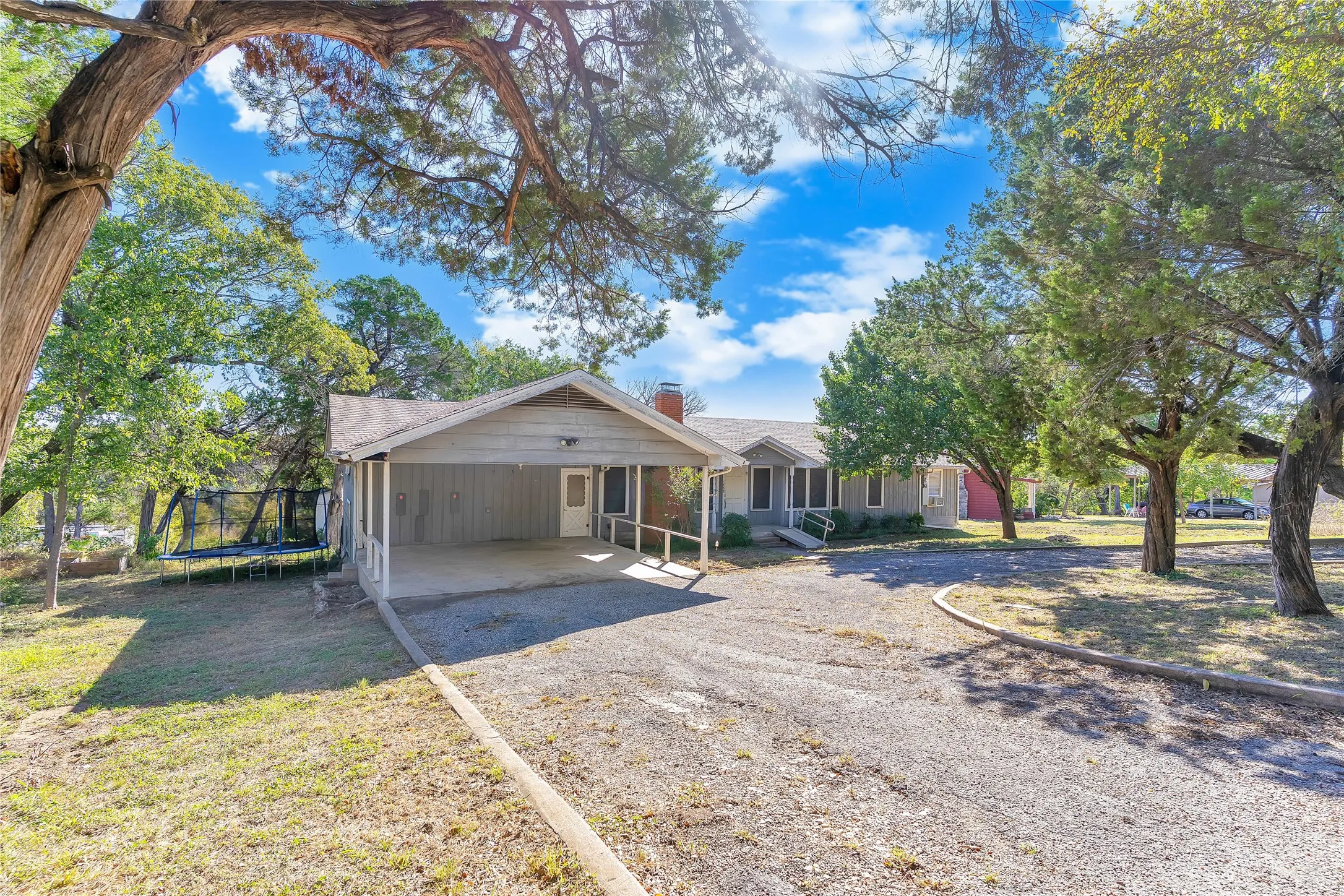 View of front of property featuring a trampoline, driveway, a chimney, a patio area, and a carport