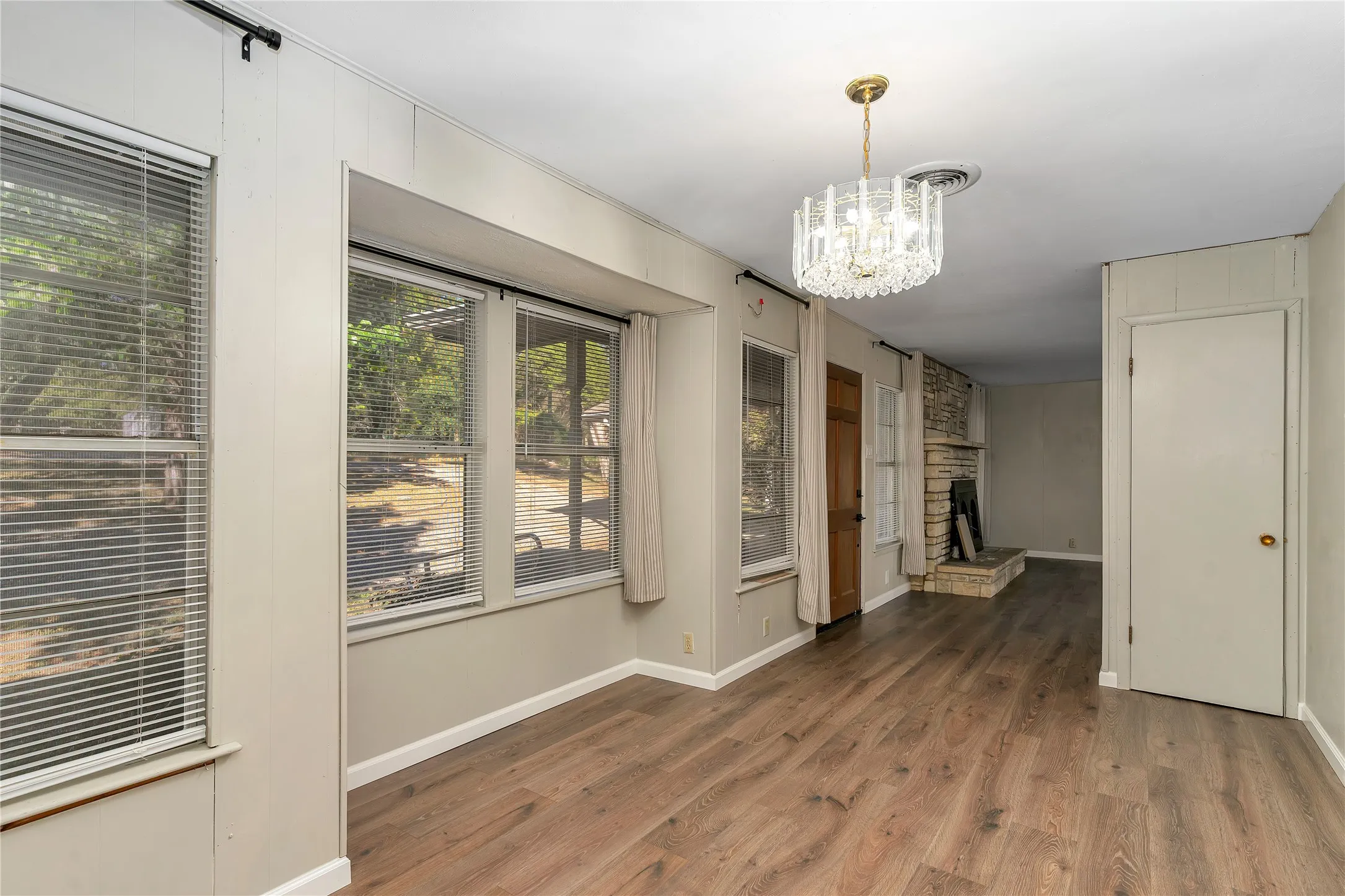 Unfurnished dining area featuring a chandelier, a stone fireplace, and wood finished floors