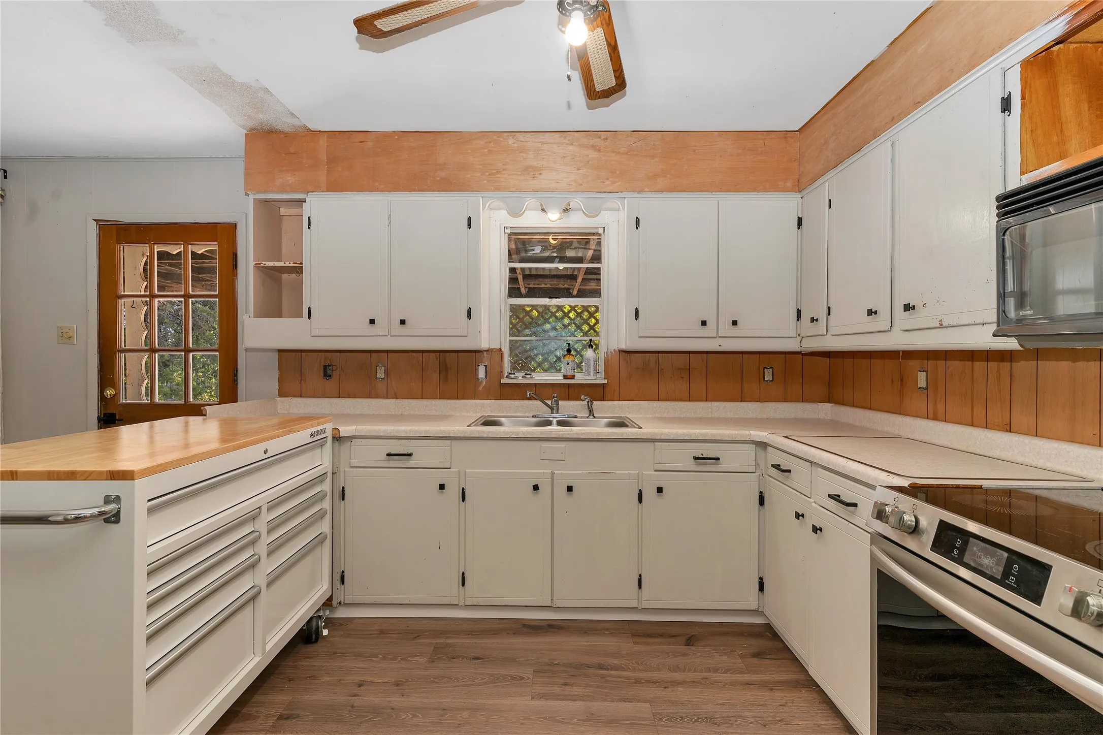 Kitchen featuring a peninsula, stainless steel range with electric stovetop, light wood finished floors, ceiling fan, and black microwave