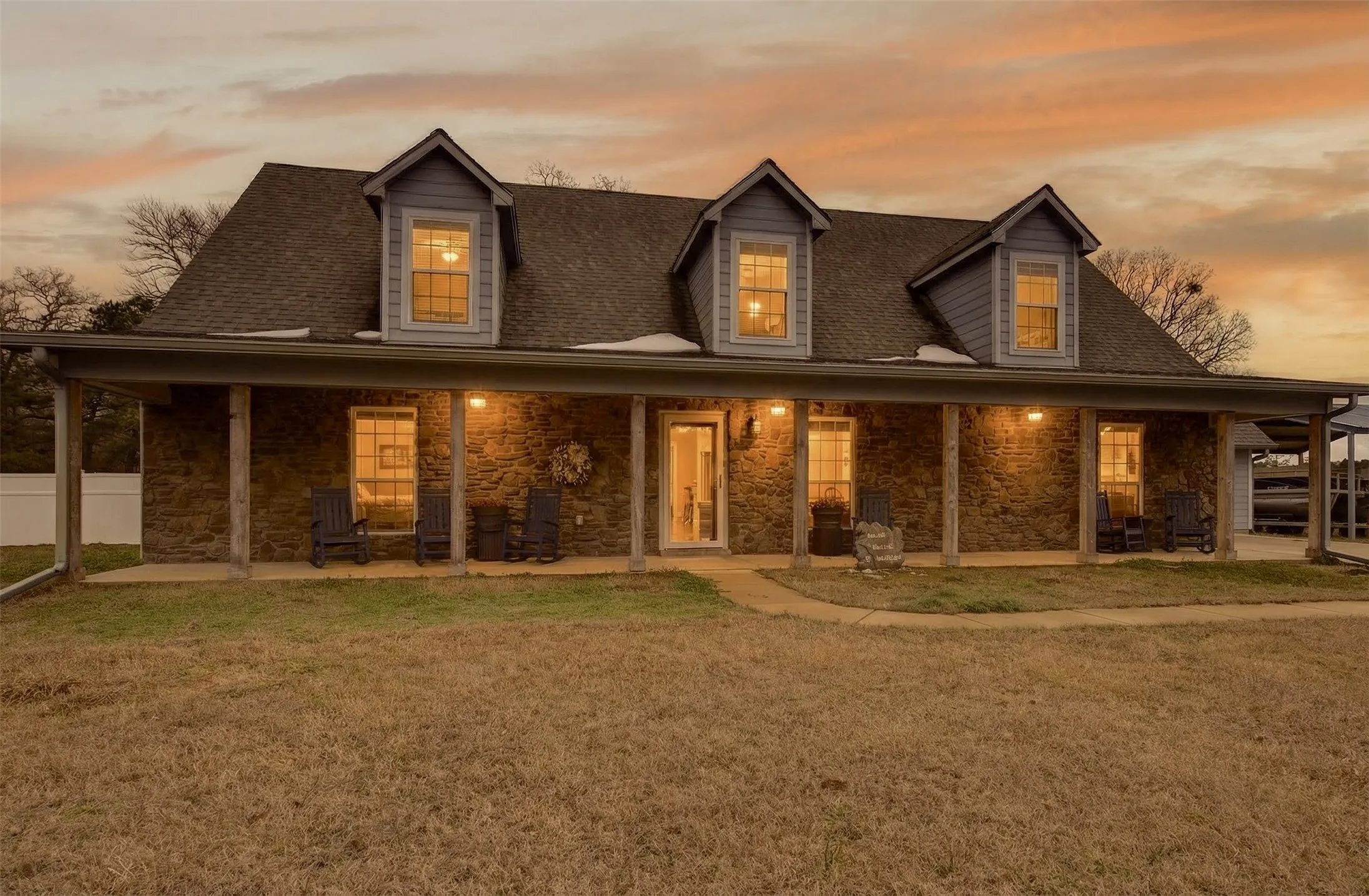 View of front of house with stone siding, covered porch, a lawn, and roof with shingles