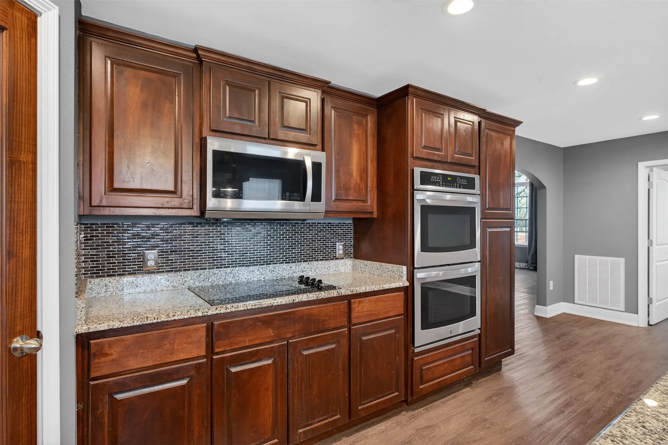Kitchen with arched walkways, light stone counters, stainless steel appliances, dark wood-style floors, and recessed lighting