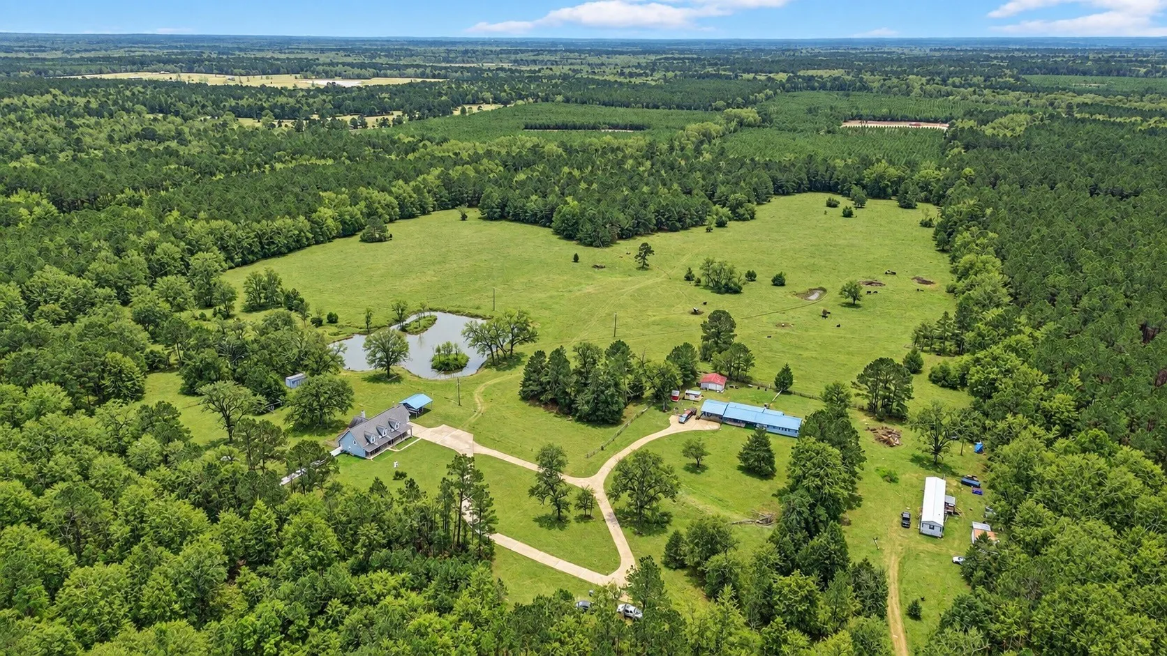 Expansive property featuring a sizable pond, multiple structures, and extensive wooded areas