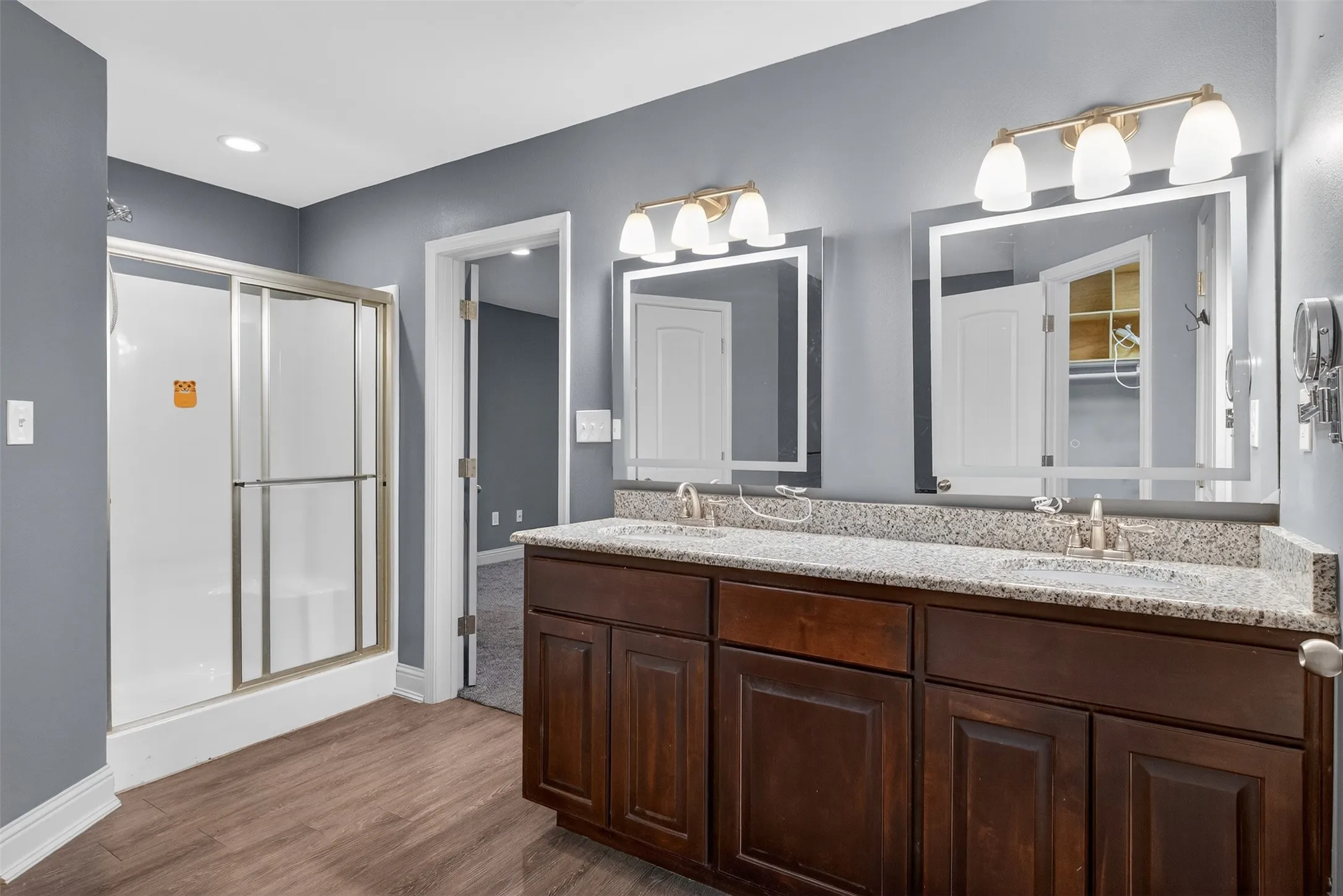 Full bath featuring a stall shower, double vanity, and dark wood-style floors