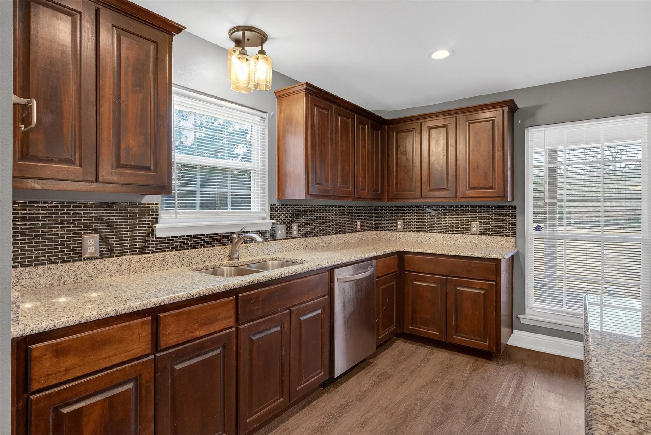 Kitchen with light stone countertops, dark wood-type flooring, dishwasher, dark wood finish cabinetry, and tasteful backsplash