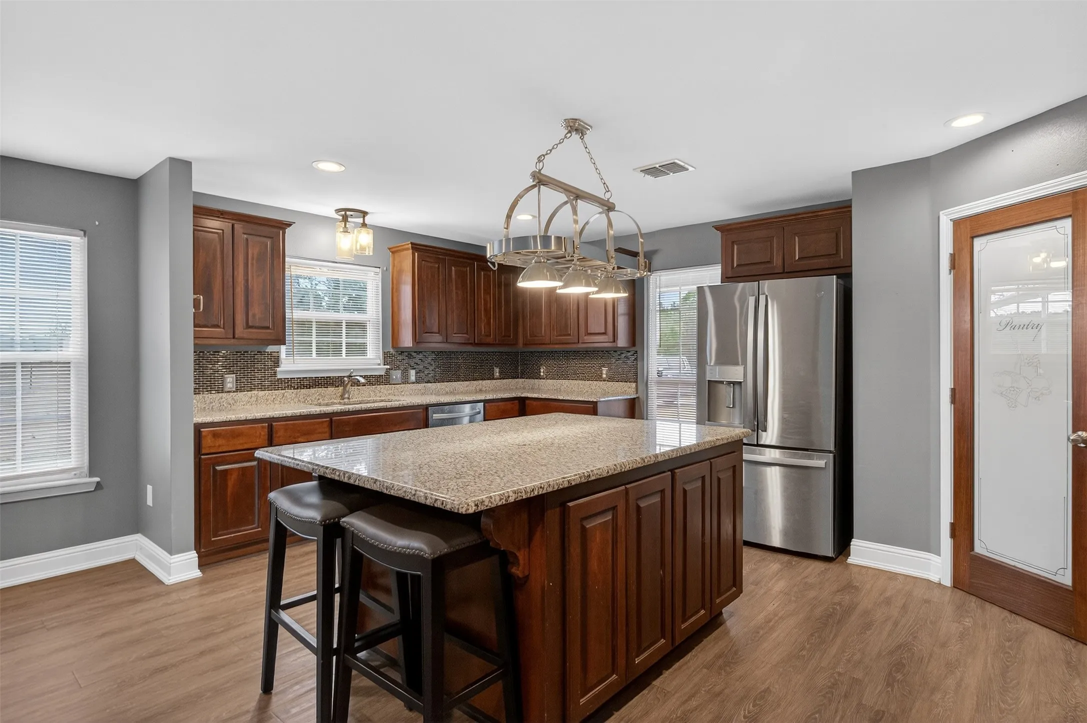 Kitchen featuring stainless steel appliances, dark wood-type flooring, dark wood finish cabinetry, a kitchen island, and light stone countertops