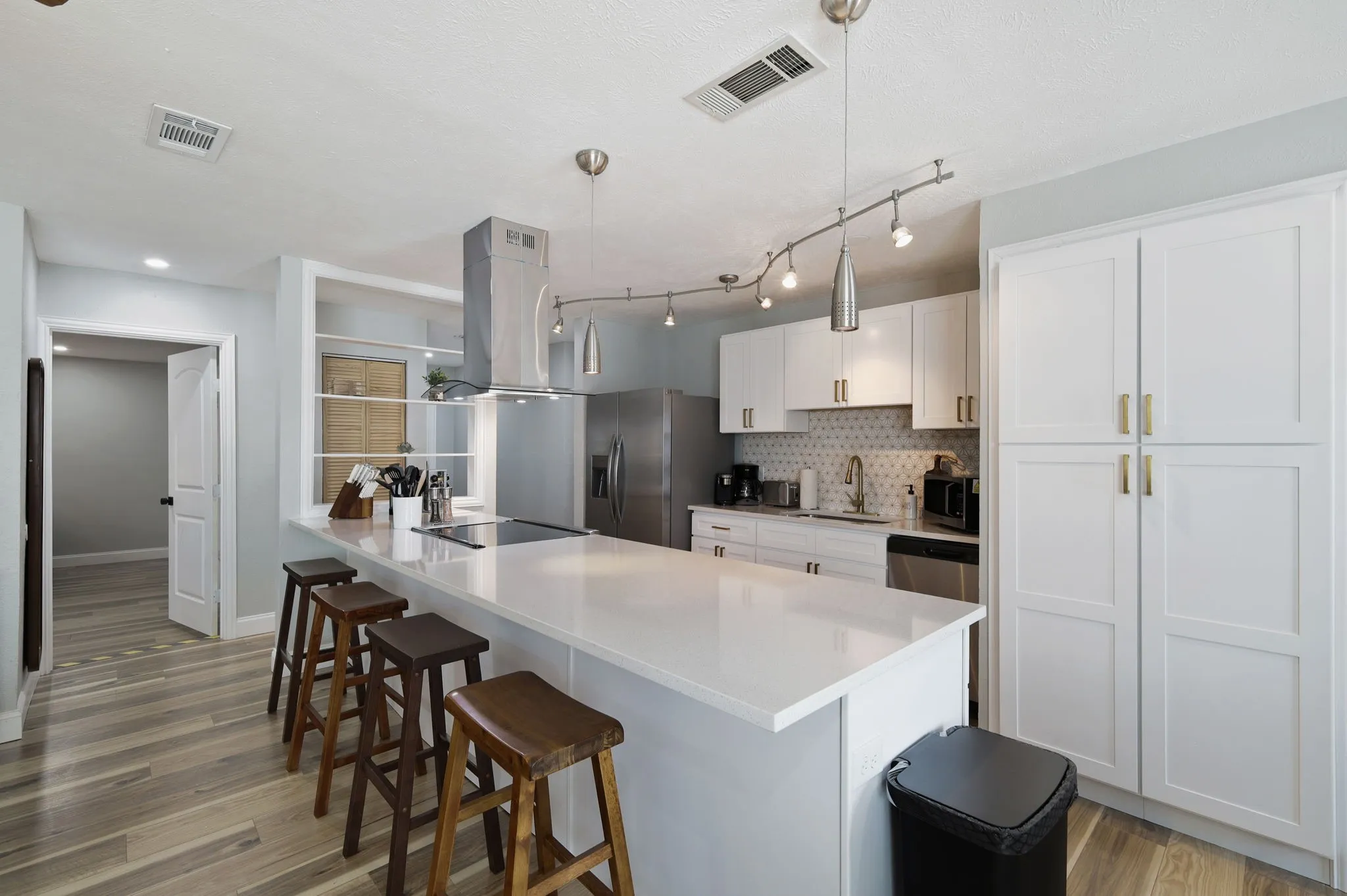 Kitchen featuring backsplash, white cabinets, sink, decorative light fixtures, and island exhaust hood