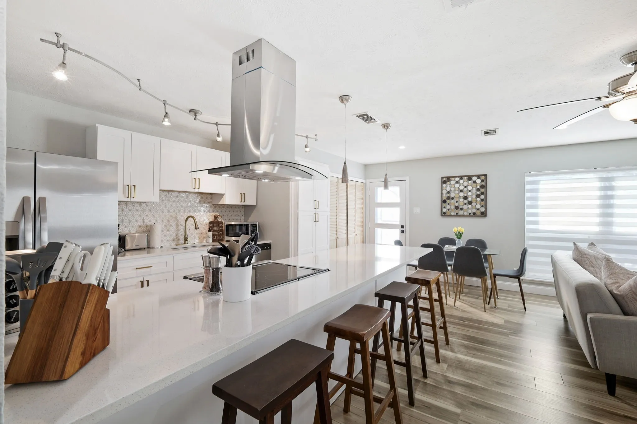 Kitchen with white cabinetry, stainless steel appliances, tasteful backsplash, island exhaust hood, and decorative light fixtures