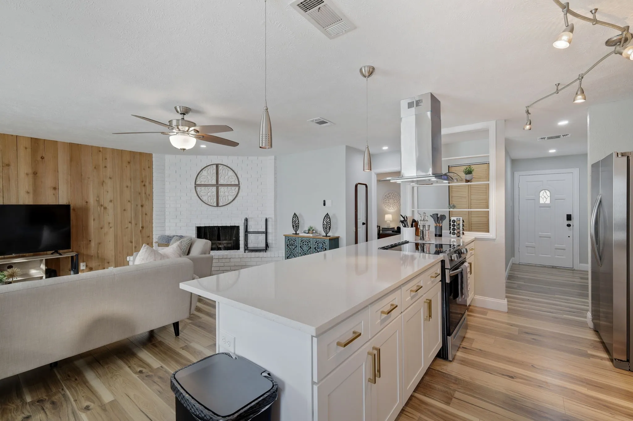 Kitchen featuring pendant lighting, a brick fireplace, white cabinetry, island exhaust hood, and stainless steel appliances