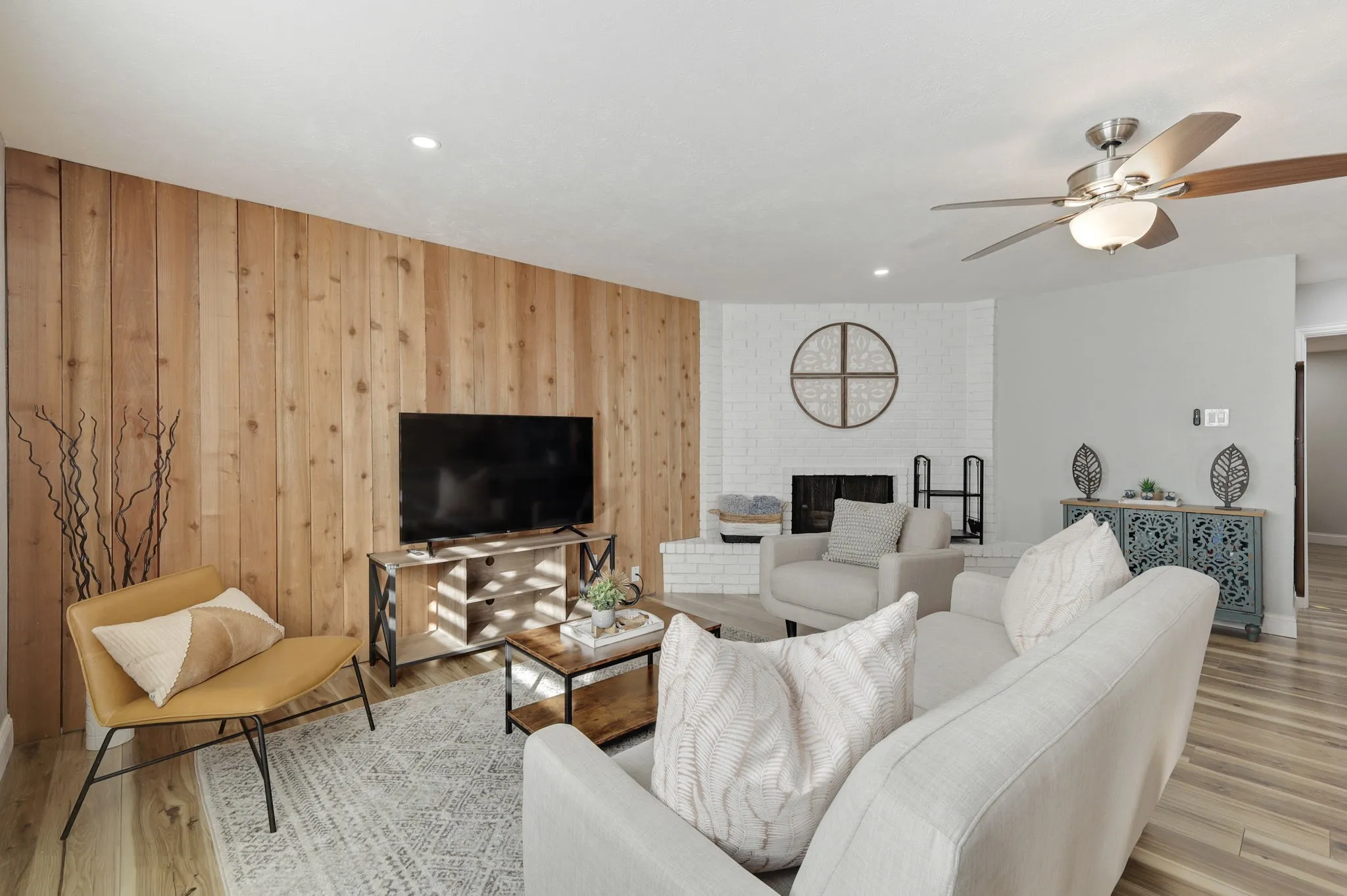 Living room with a brick fireplace, ceiling fan, wood walls, and light hardwood / wood-style flooring
