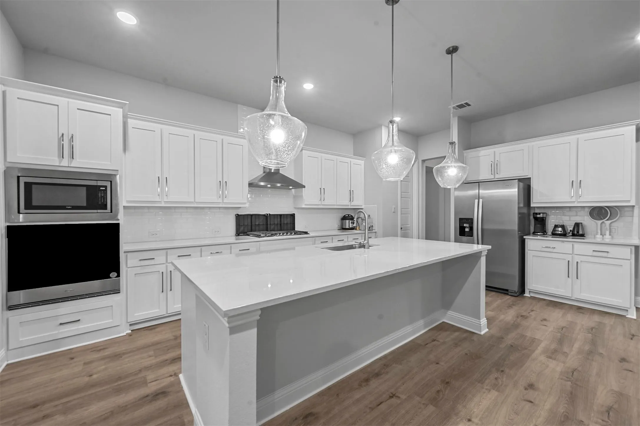 Kitchen with backsplash, stainless steel appliances, white cabinetry, and light wood flooring