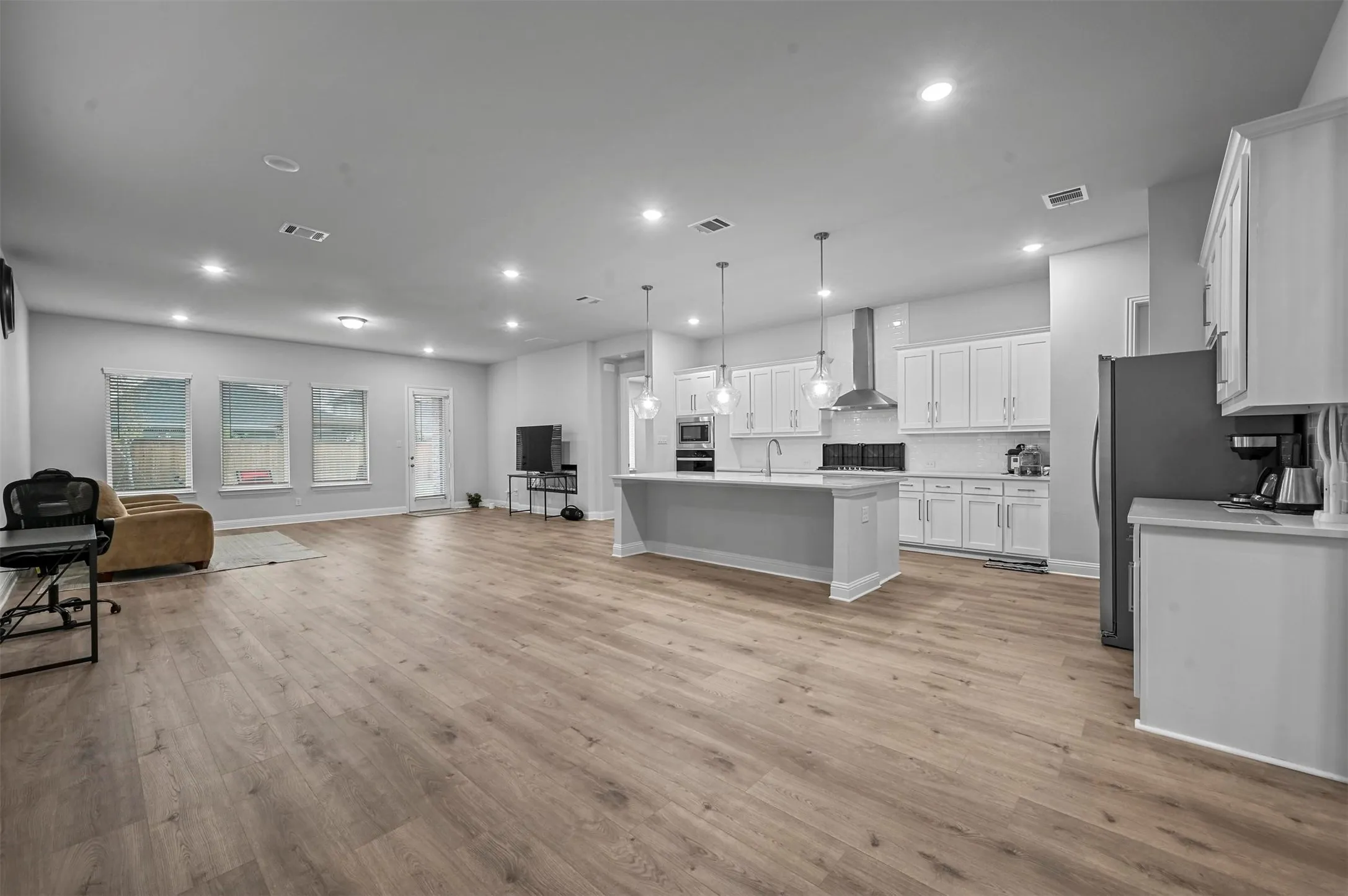 Kitchen with open floor plan, white cabinetry, an island with sink, decorative light fixtures, and light wood floors