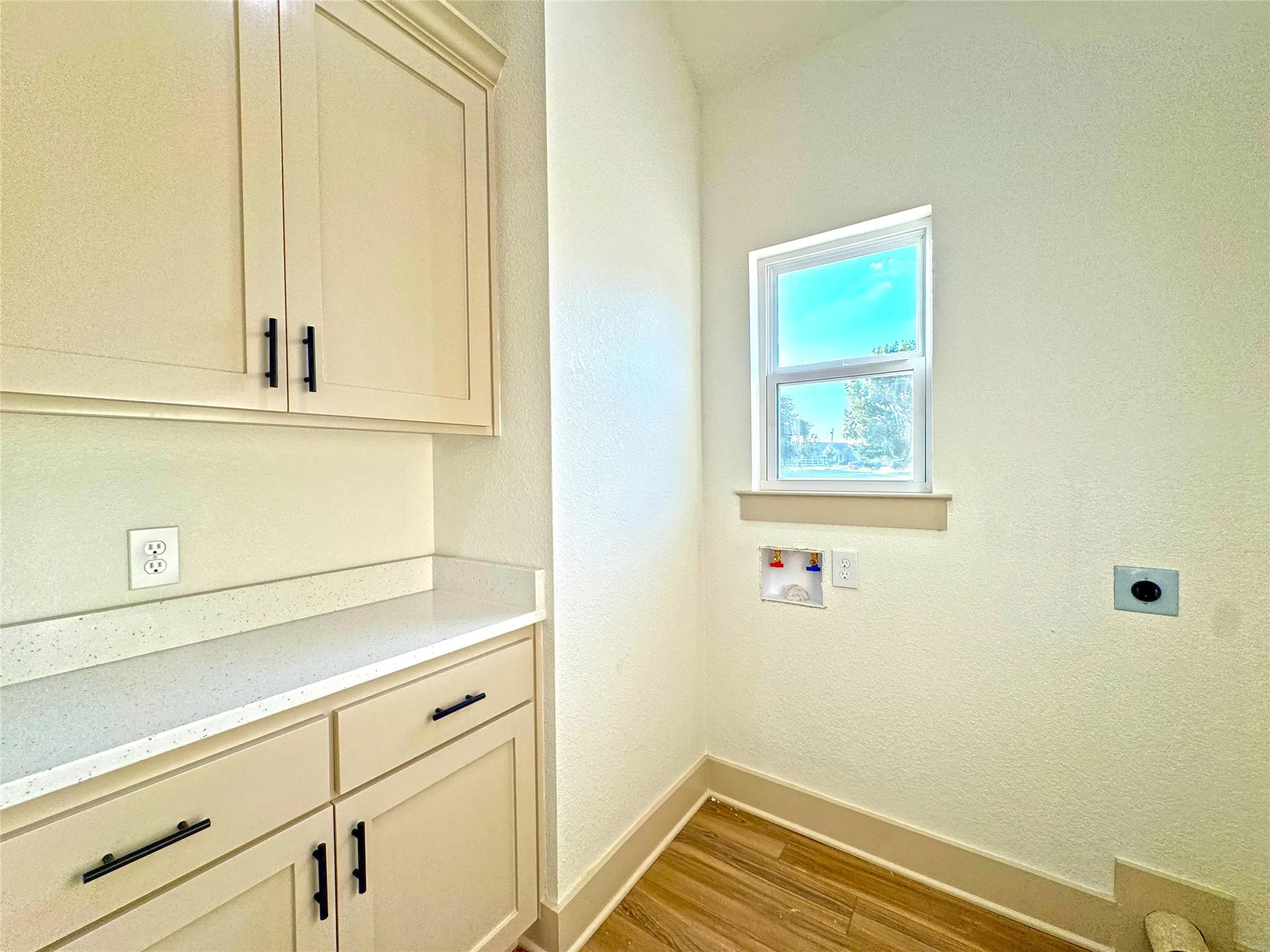 Laundry room featuring a textured wall, light wood-style floors, hookup for a washing machine, electric dryer hookup, and cabinet space