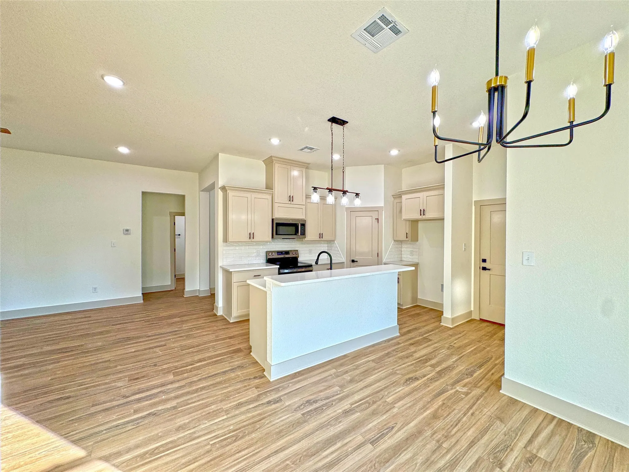 Kitchen with suspended lighting, a center island with sink, light countertops, open floor plan, and stainless steel appliances