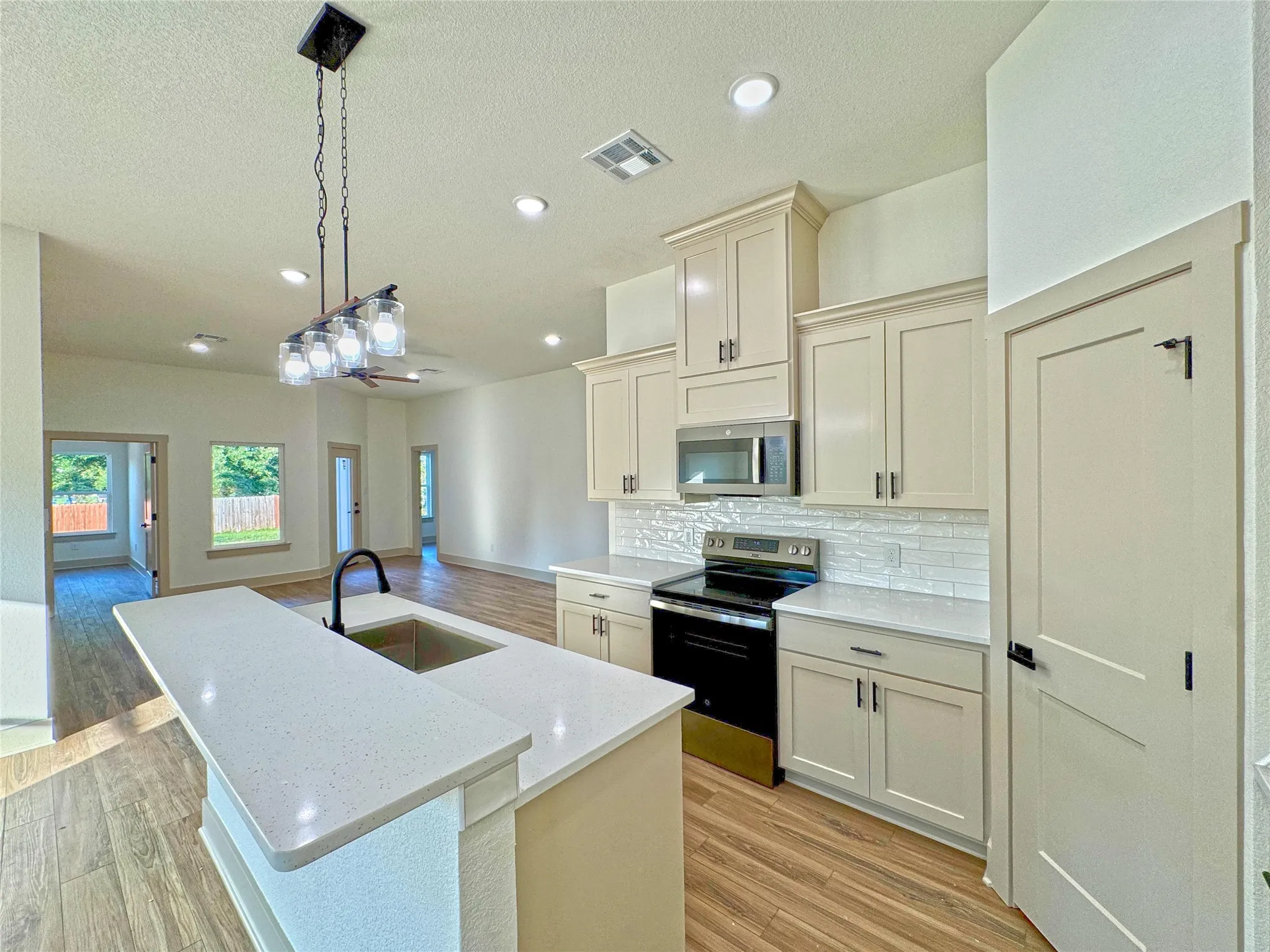 Kitchen featuring stainless steel appliances, an island with sink, light wood-style flooring, pendant lighting, and a textured ceiling