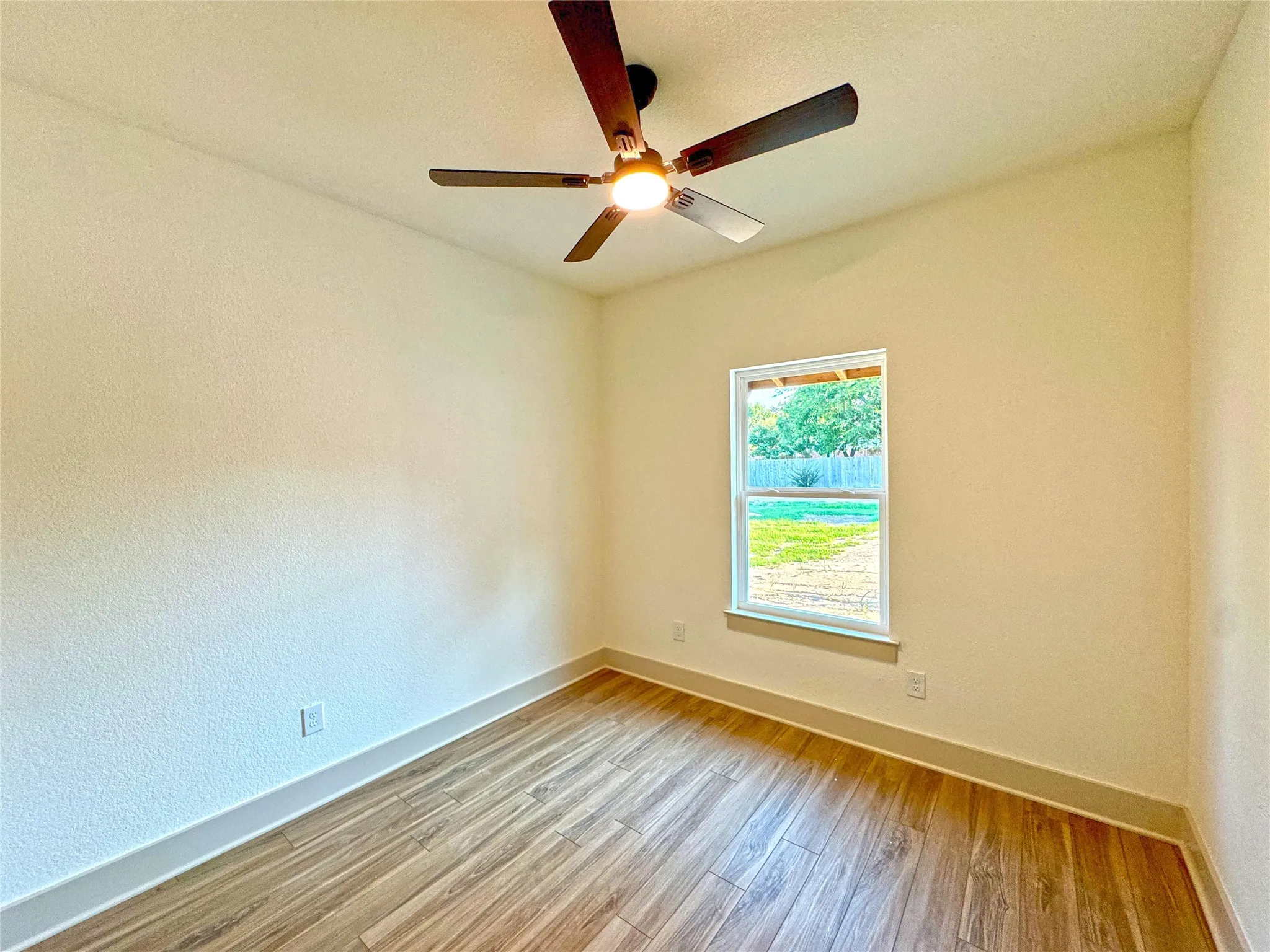 Spare room with light wood-style flooring, a ceiling fan, and a textured wall