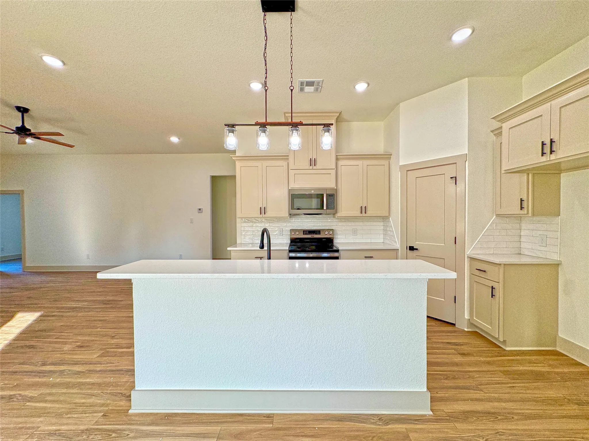 Kitchen featuring an island with sink, pendant lighting, stainless steel appliances, light wood-style floors, and a textured ceiling