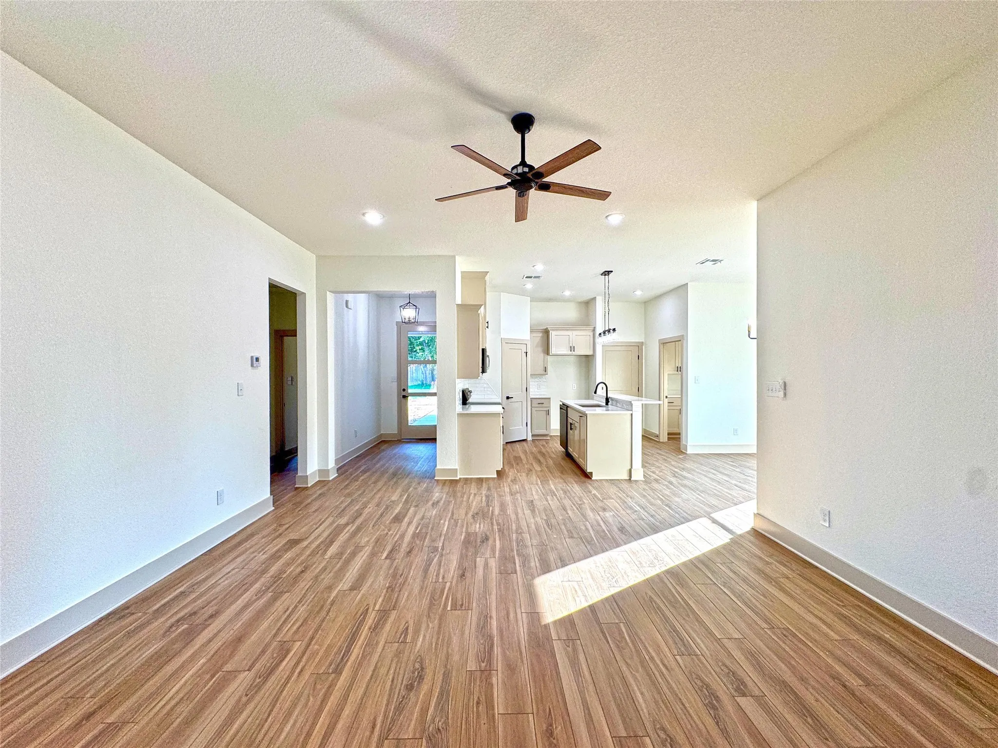 Unfurnished living room featuring light wood-style floors, a ceiling fan, and a textured ceiling
