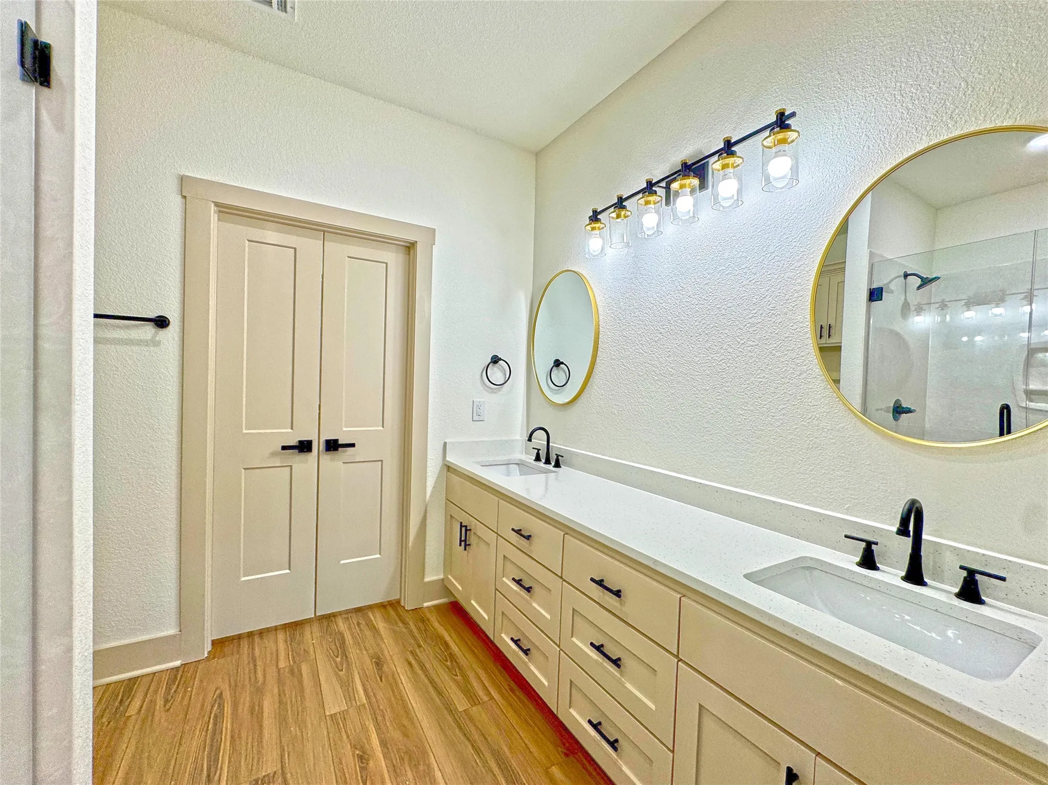 Full bathroom featuring a textured wall, a stall shower, light wood-style flooring, and double vanity
