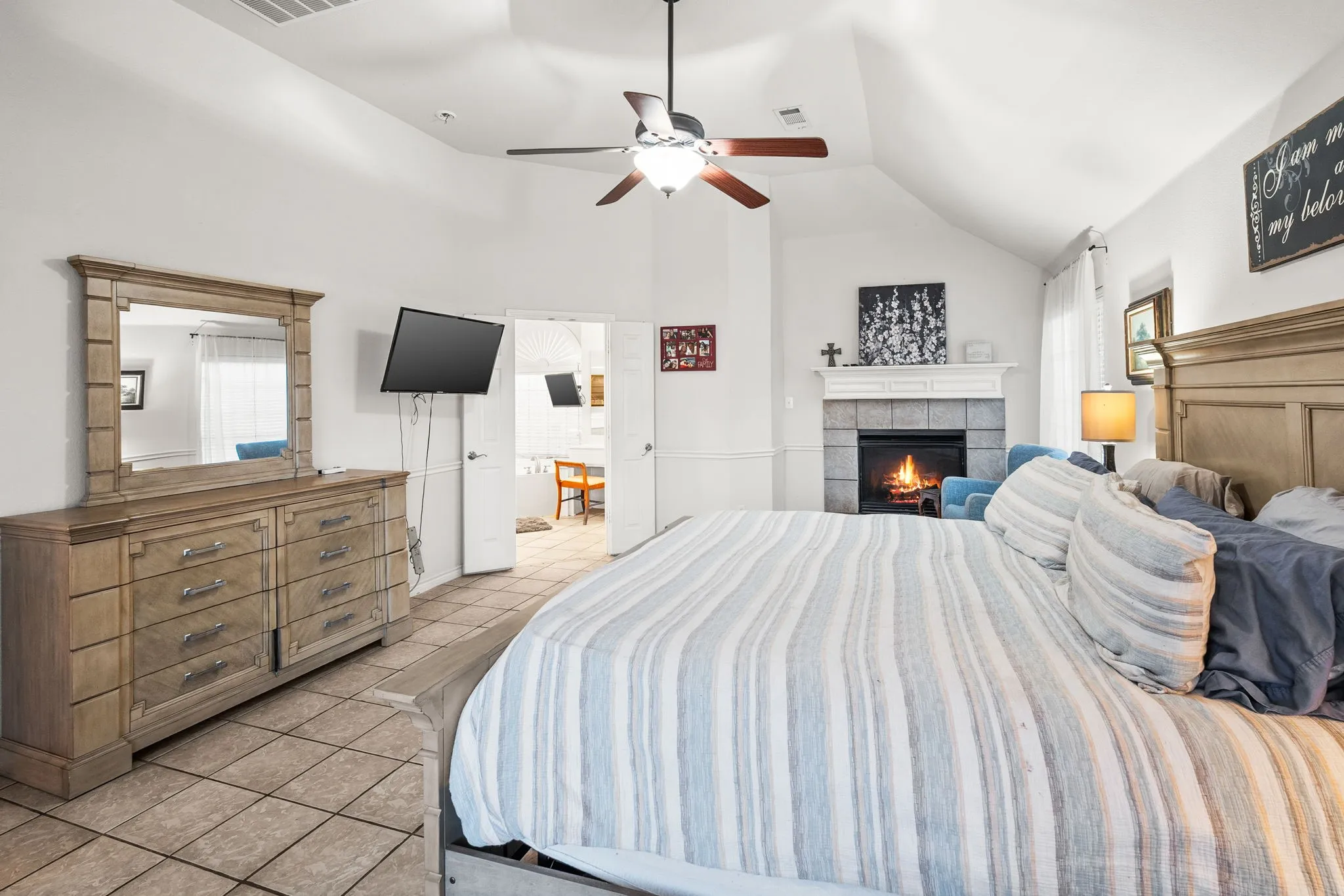 Bedroom featuring a ceiling fan, lofted ceiling, light tile patterned floors, and a tile fireplace