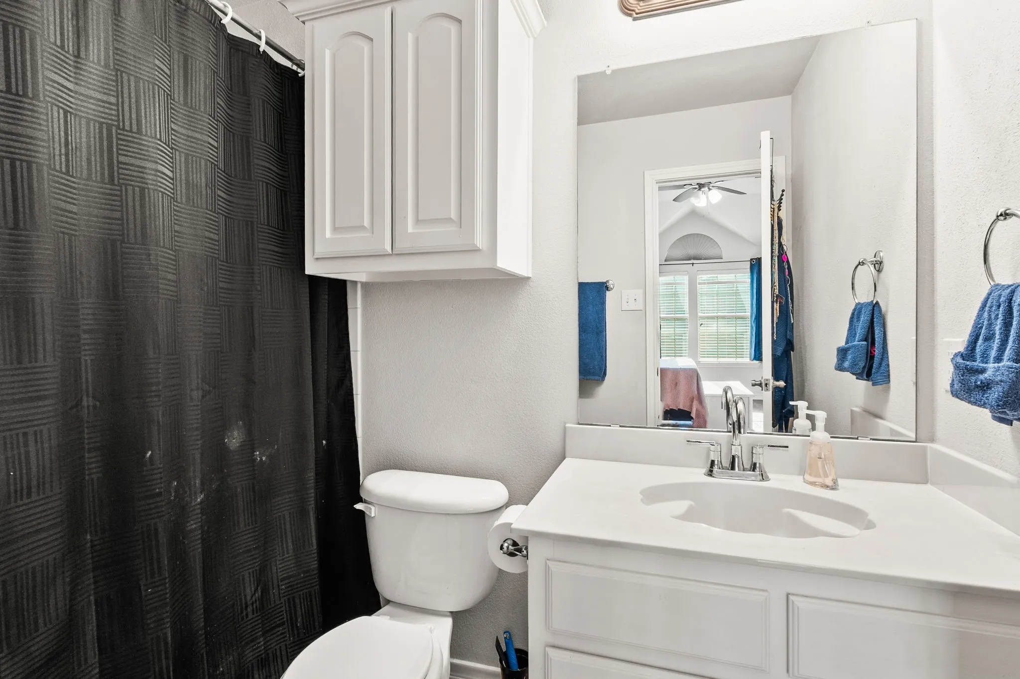 Bathroom with vanity, curtained shower, a textured wall, and a ceiling fan