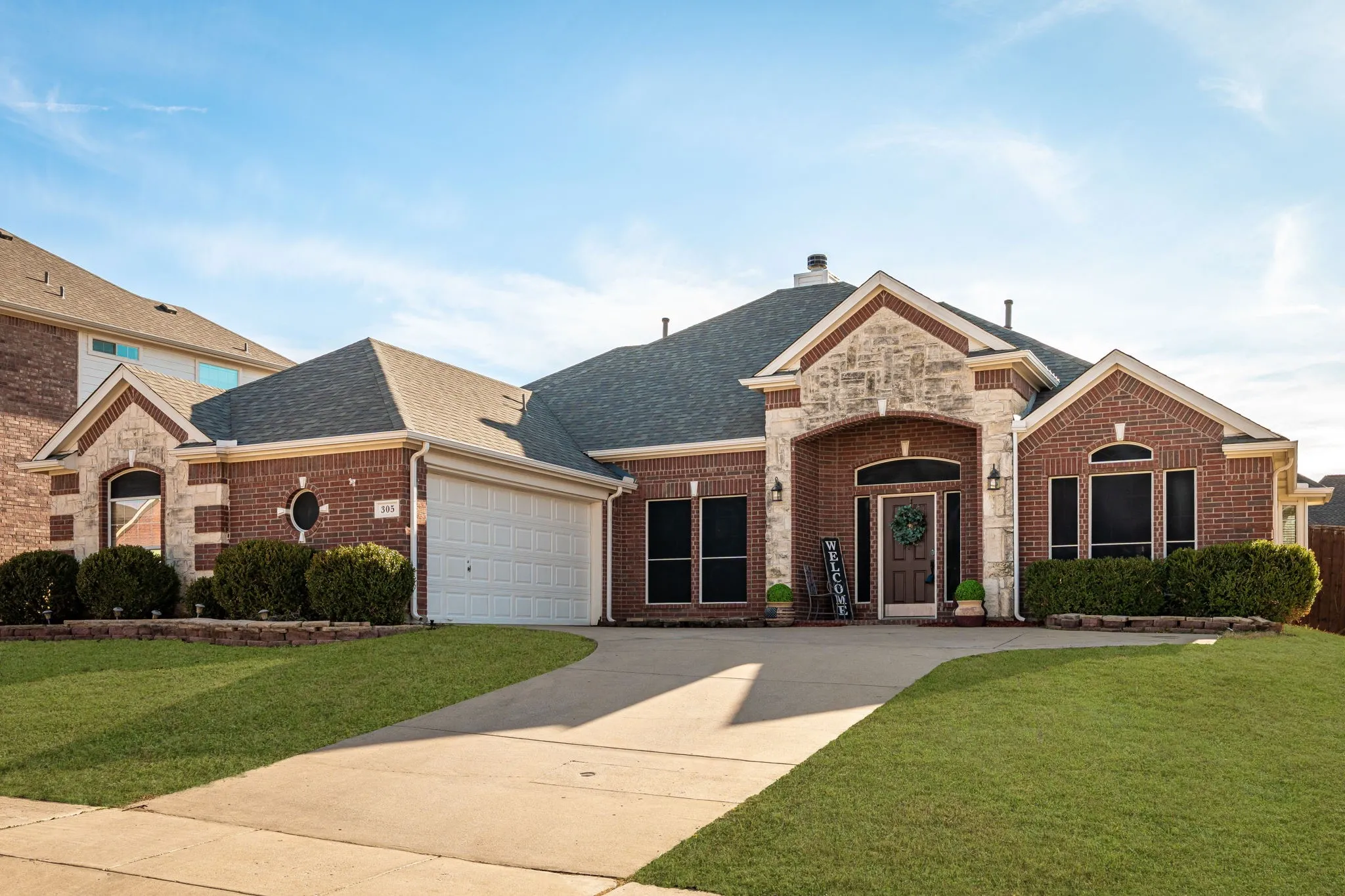 French country style house with a shingled roof, brick siding, a front lawn, and concrete driveway