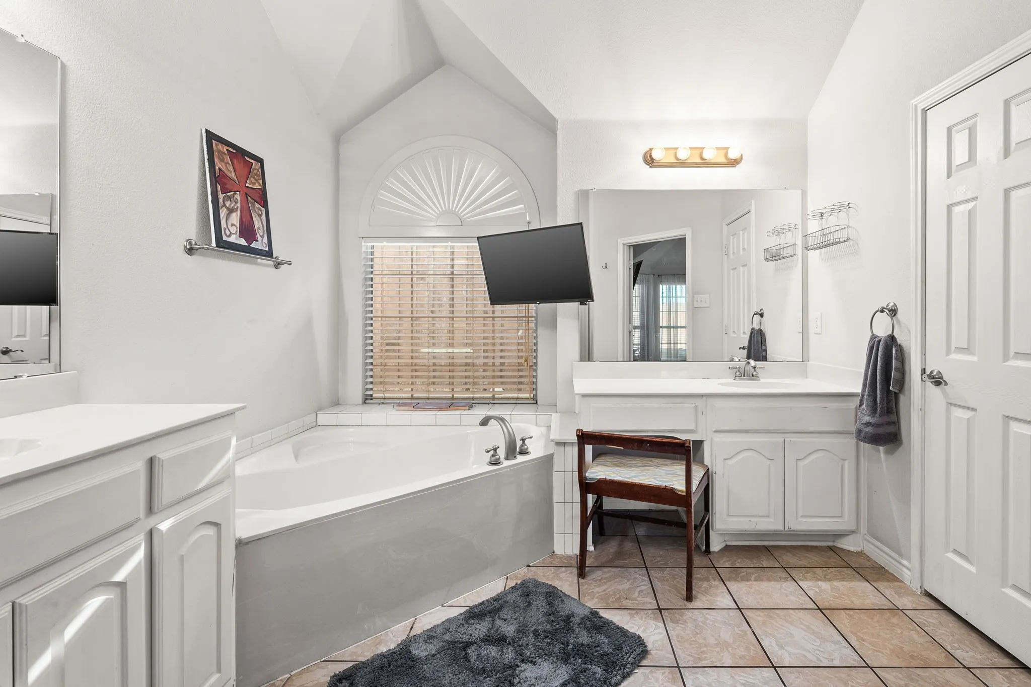 Bathroom with two vanities, lofted ceiling, a bath, plenty of natural light, and light tile patterned flooring
