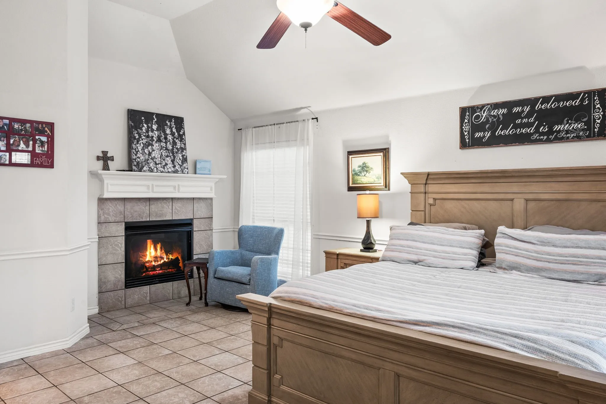 Bedroom featuring light tile patterned floors, vaulted ceiling, a tiled fireplace, and a ceiling fan