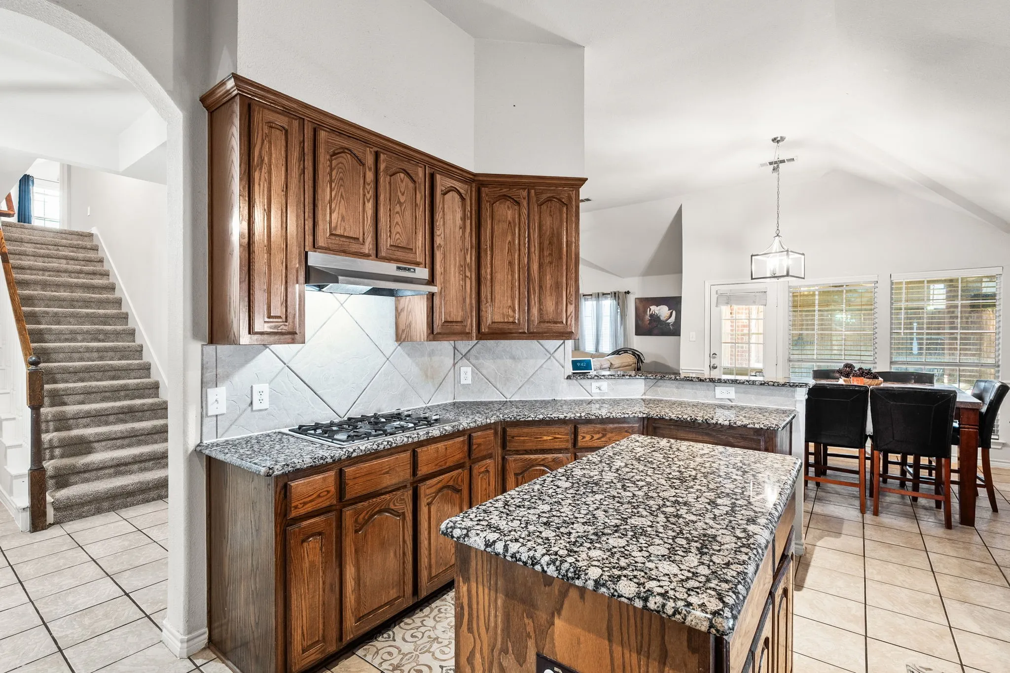Kitchen featuring dark stone countertops, hanging light fixtures, light tile patterned flooring, tasteful backsplash, and lofted ceiling