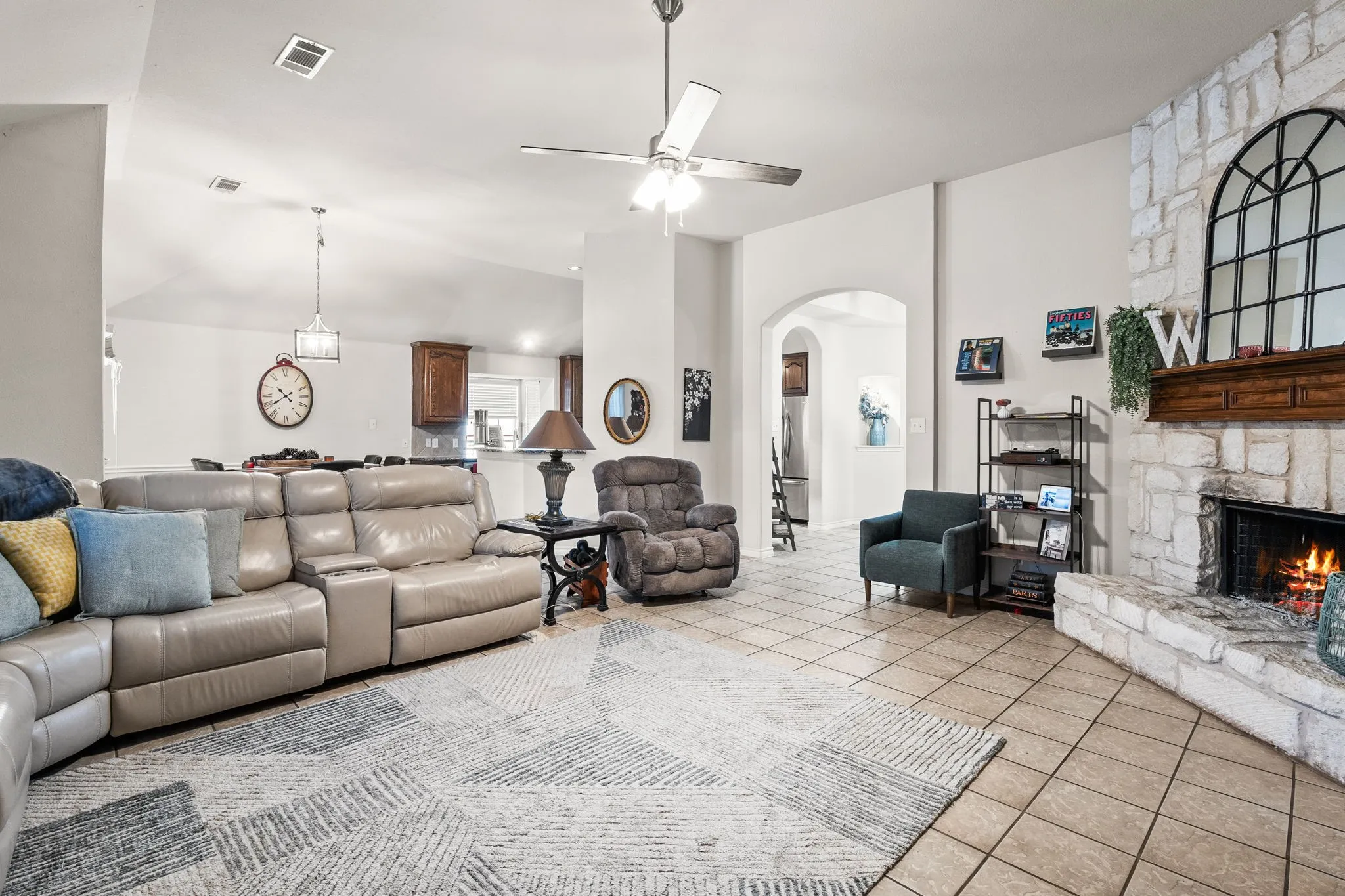 Living area featuring tile patterned flooring, a stone fireplace, arched walkways, a ceiling fan, and lofted ceiling