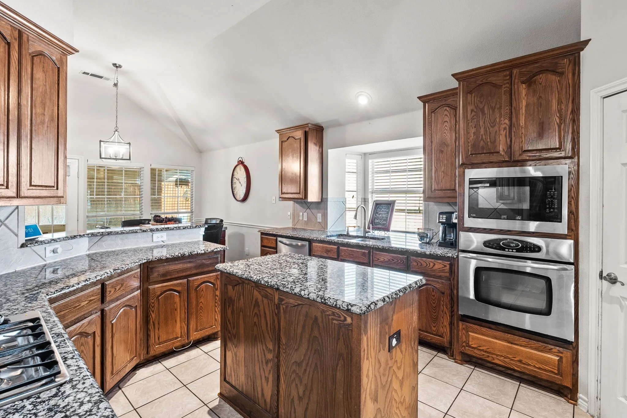 Kitchen featuring dark stone counters, stainless steel appliances, a center island, light tile patterned flooring, and decorative light fixtures