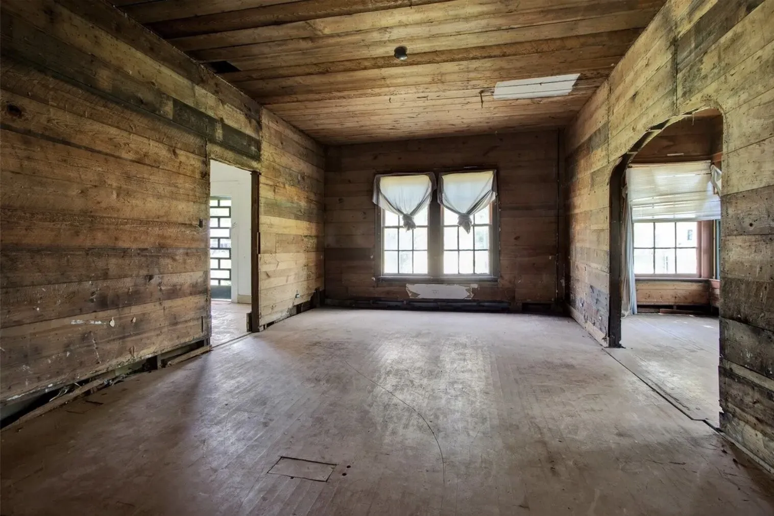 Empty room with wooden ceiling, healthy amount of natural light, arched walkways, and wooden walls