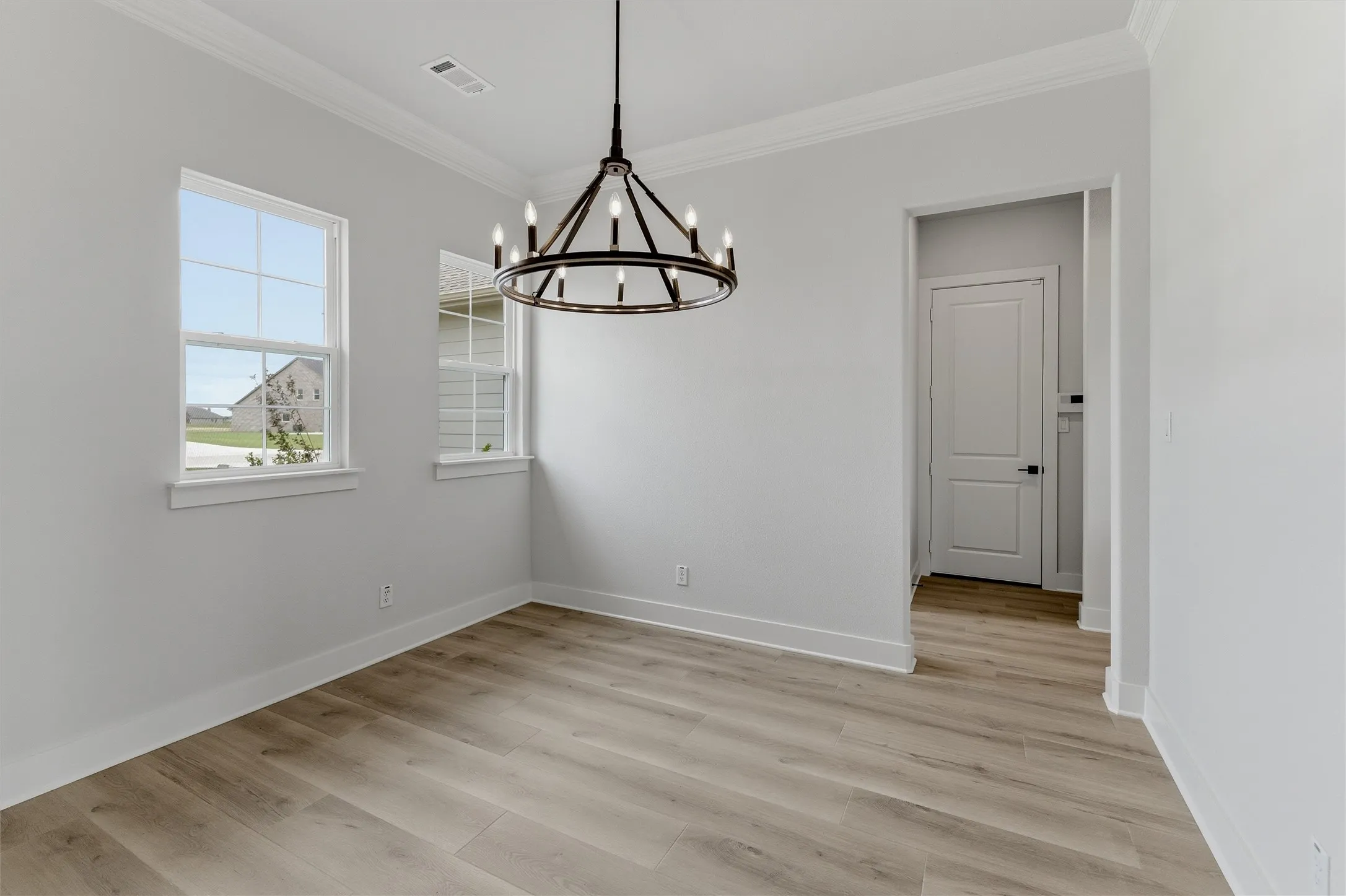 Room featuring wood-finish flooring, two windows with white trim, a contemporary black metal chandelier, and a doorway with a panel door