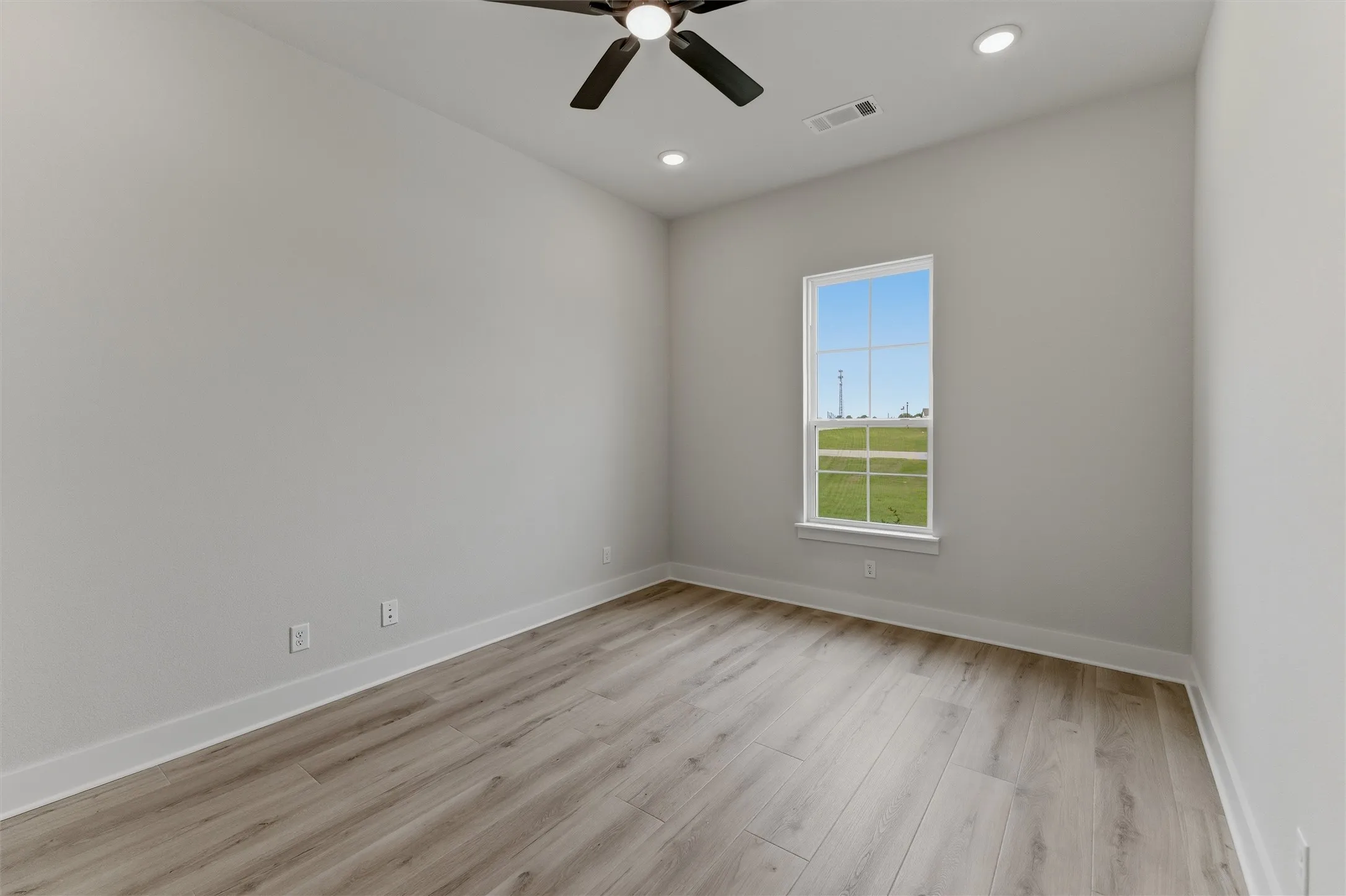 Bright interior space featuring a window with exterior views, wood-finish flooring, a ceiling fan, and recessed lighting