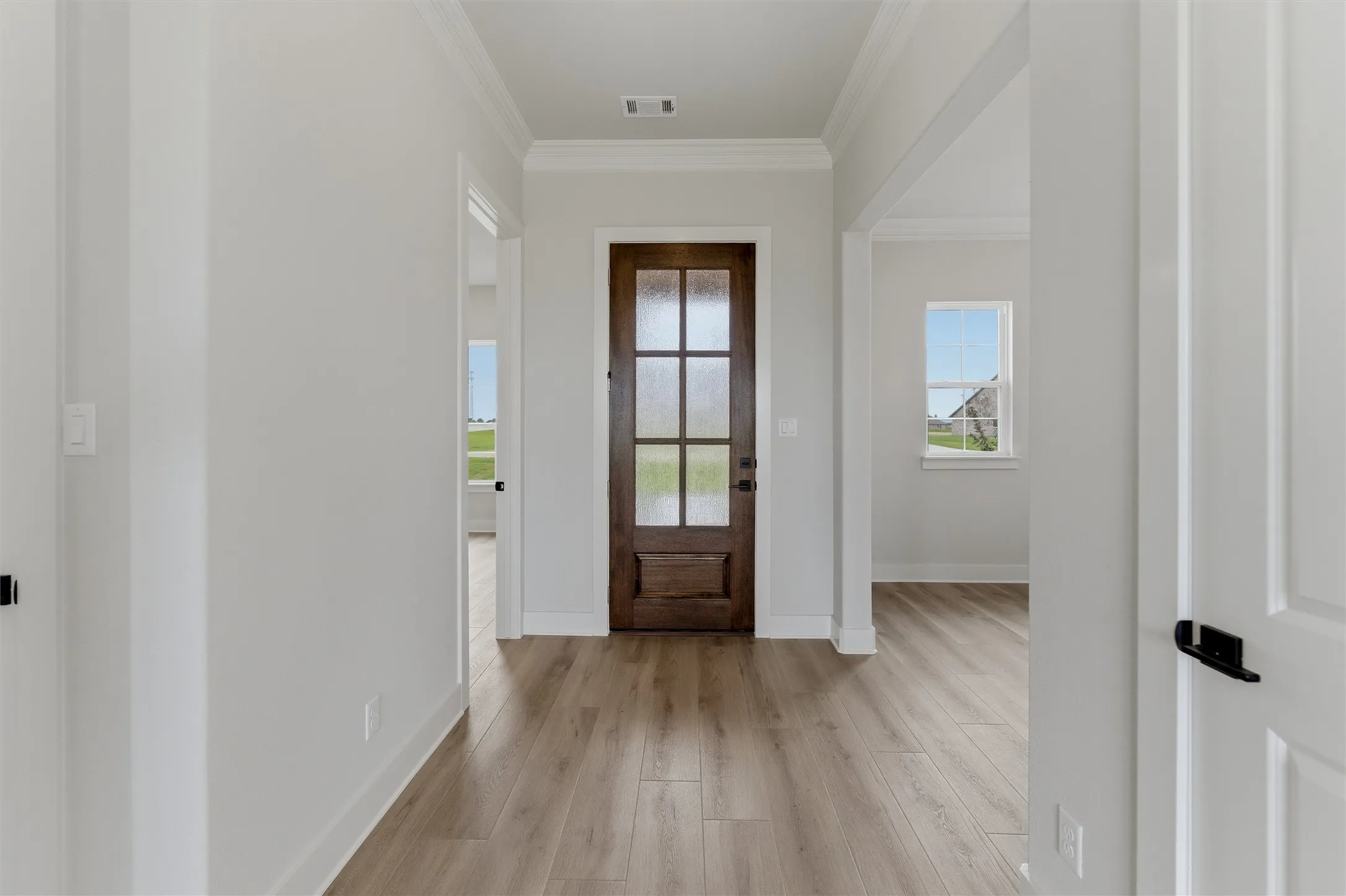 Entryway featuring a dark wood door with frosted glass panes, light wood-finish flooring, white baseboards, crown molding, and light gray wall paint
