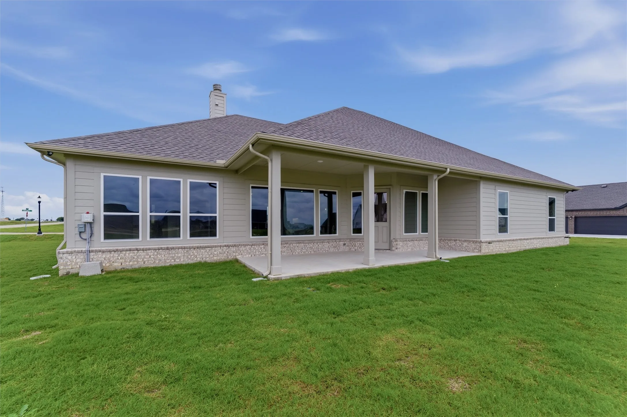 Rear elevation featuring a covered patio with columns, multiple large windows, and a chimney