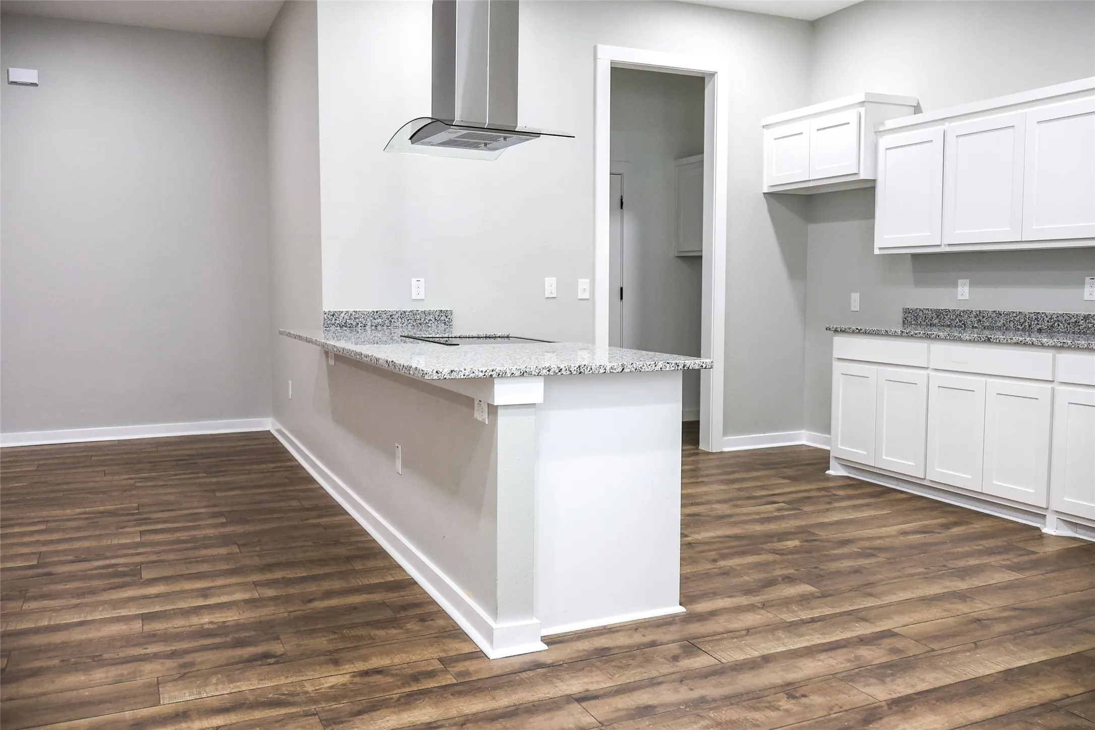 Kitchen with exhaust hood, light stone counters, dark wood finished floors, a peninsula, and white cabinetry