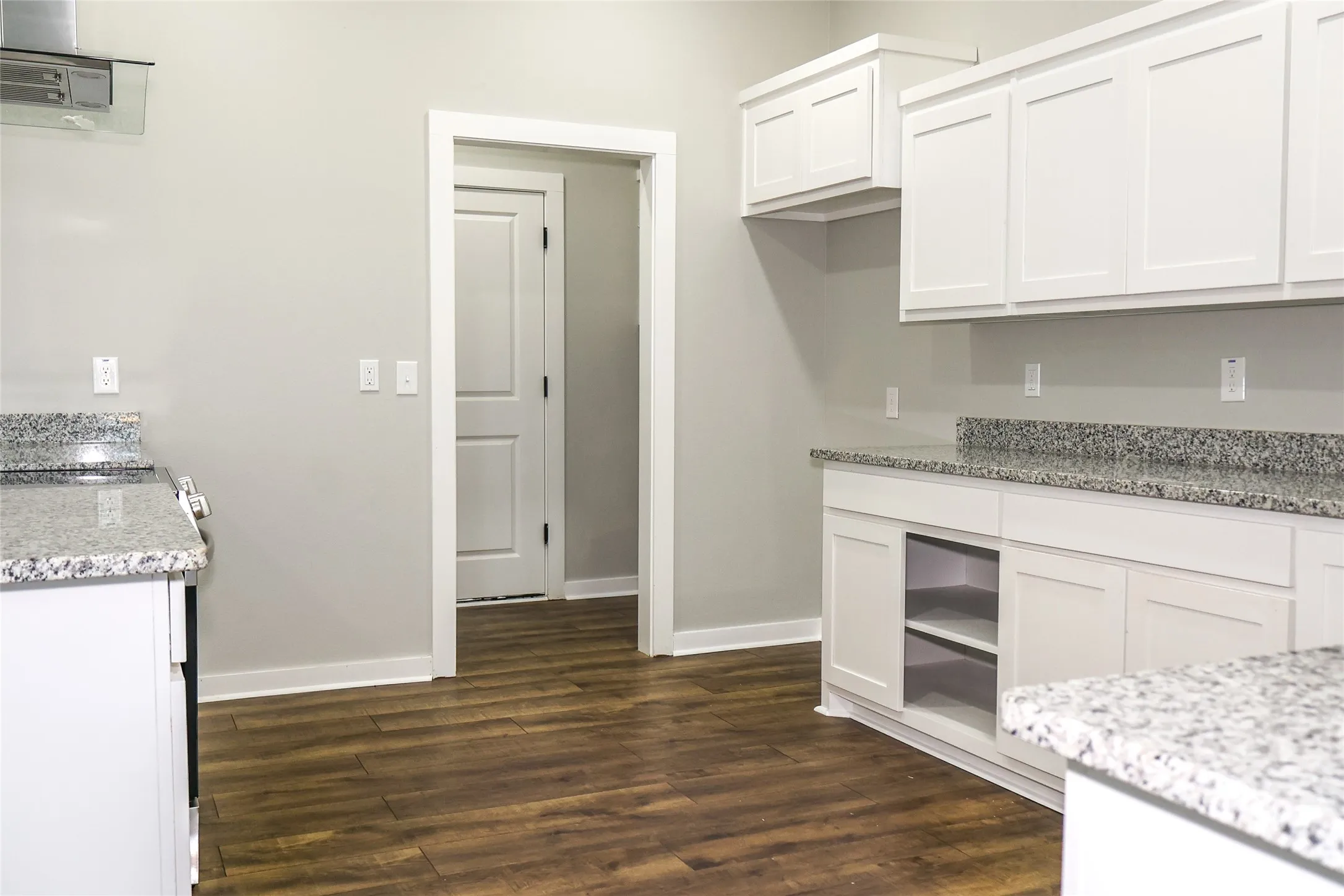 Kitchen with light stone counters, dark wood finished floors, and white cabinetry