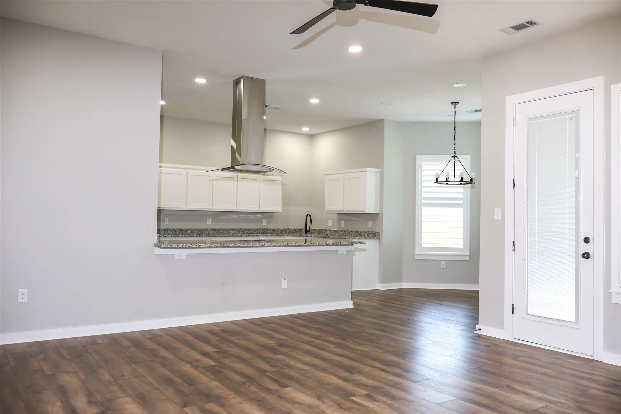 Kitchen featuring white cabinets, island range hood, dark wood-type flooring, ceiling fan, and hanging lights