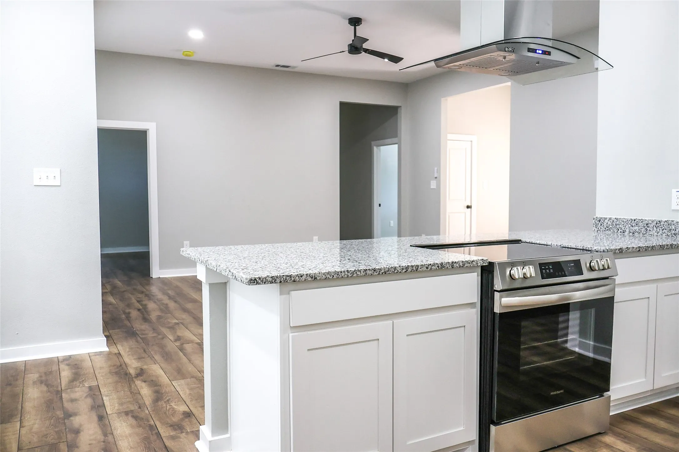 Kitchen with stainless steel range with electric cooktop, island range hood, light stone counters, dark wood-style floors, and a peninsula