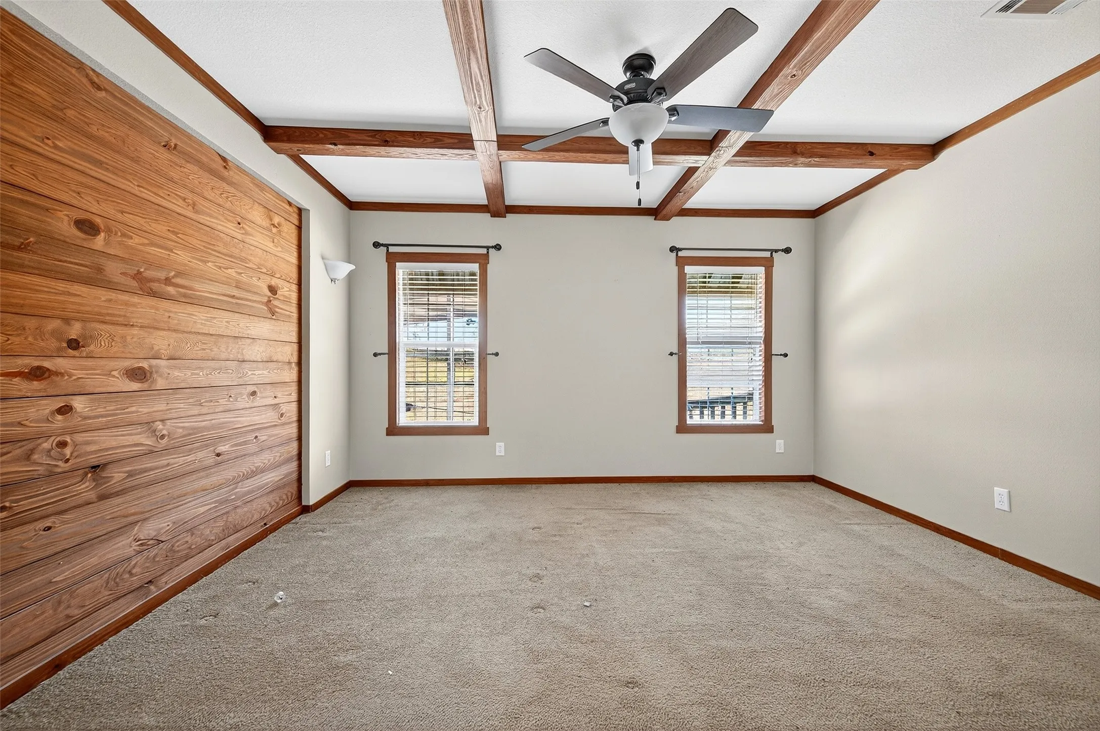 Spare room featuring beamed ceiling, healthy amount of natural light, ceiling fan, coffered ceiling, and light colored carpet