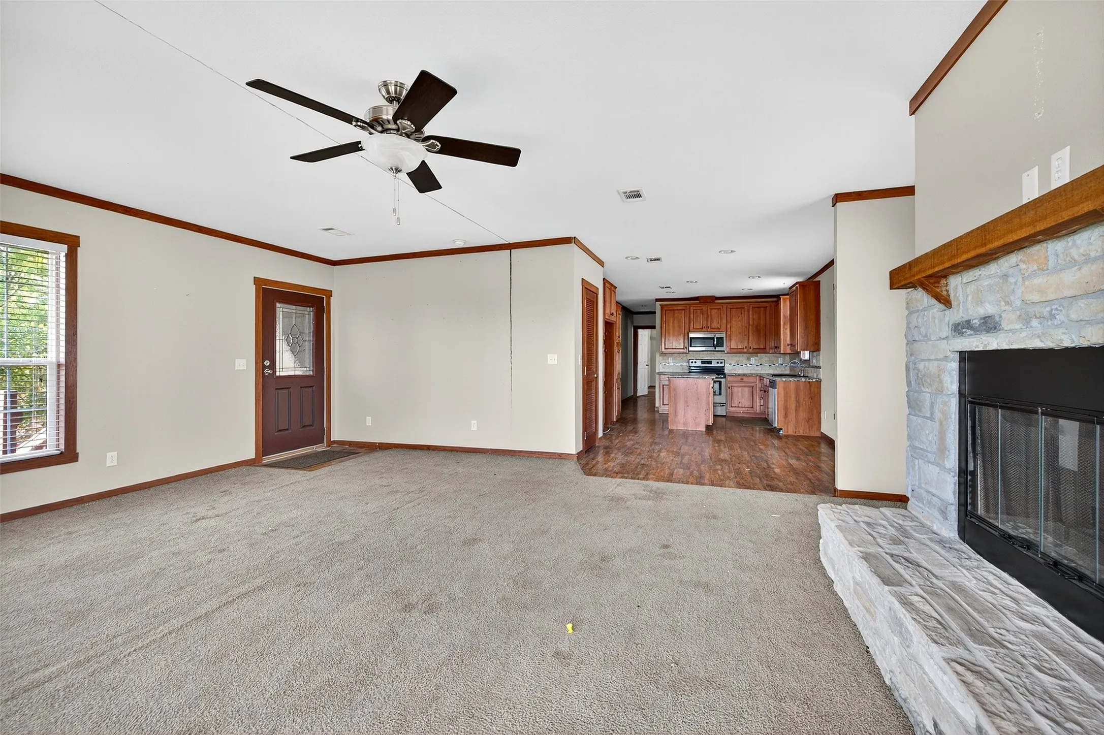 Unfurnished living room featuring ornamental molding, a fireplace, dark carpet, and a ceiling fan
