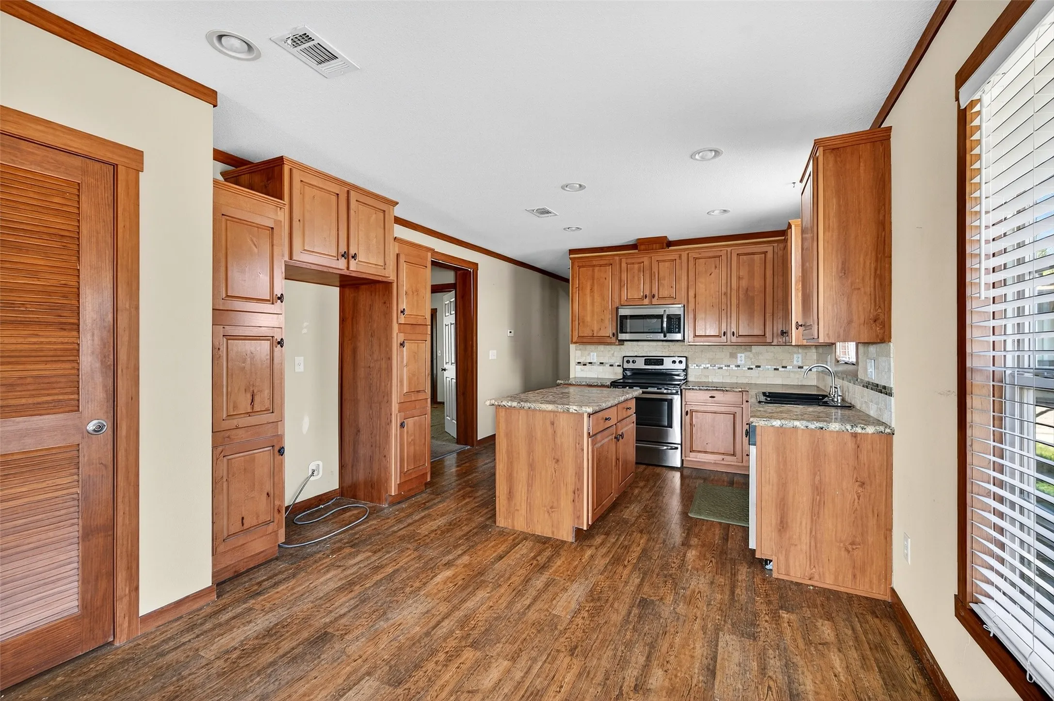 Kitchen featuring ornamental molding, brown cabinets, appliances with stainless steel finishes, dark wood-style flooring, and a kitchen island