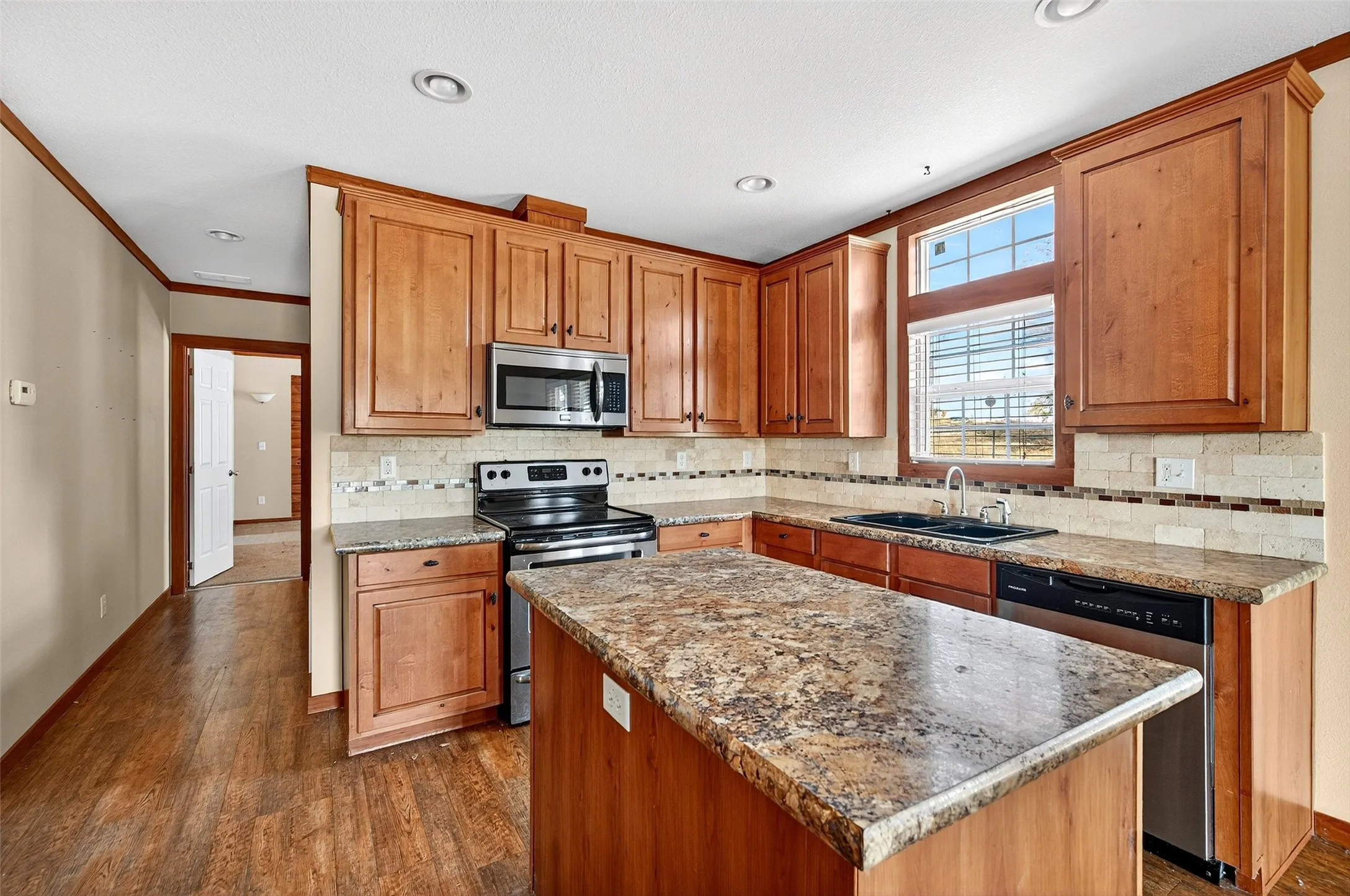 Kitchen featuring stainless steel appliances, backsplash, dark wood-style flooring, a kitchen island, and brown cabinetry
