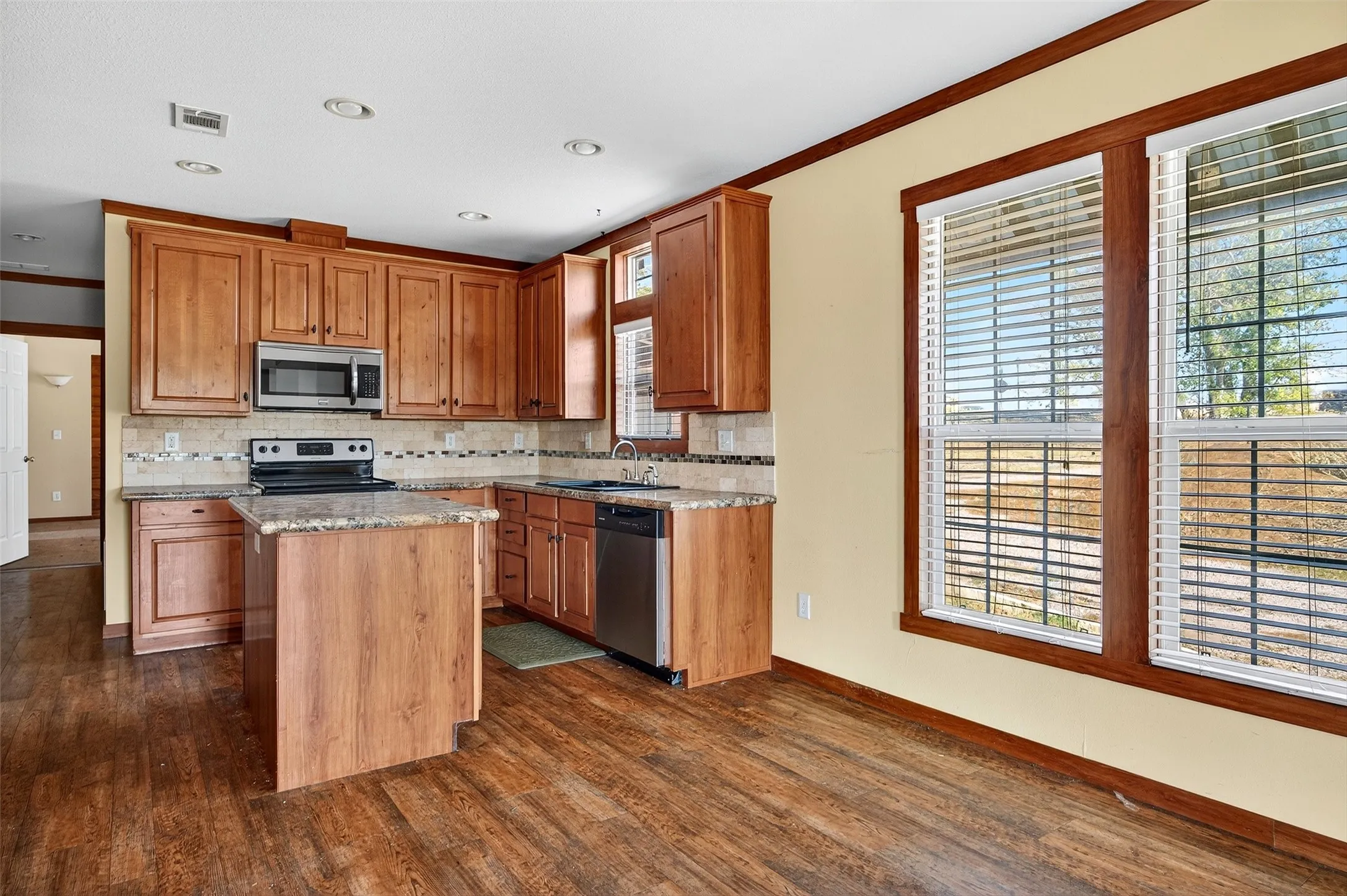 Kitchen with light stone countertops, crown molding, stainless steel appliances, backsplash, and dark wood-style flooring