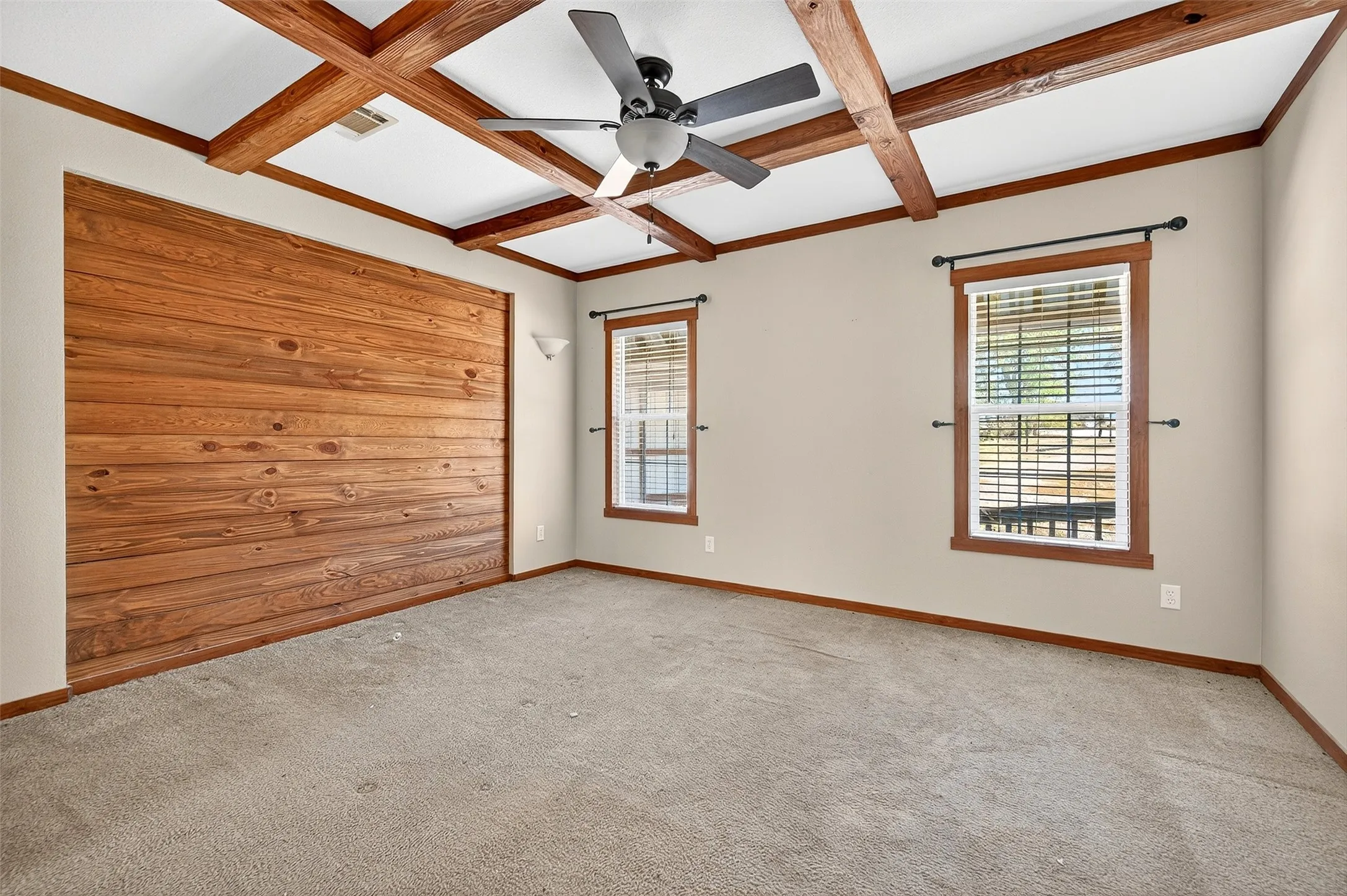 Carpeted empty room featuring coffered ceiling, beam ceiling, and a ceiling fan
