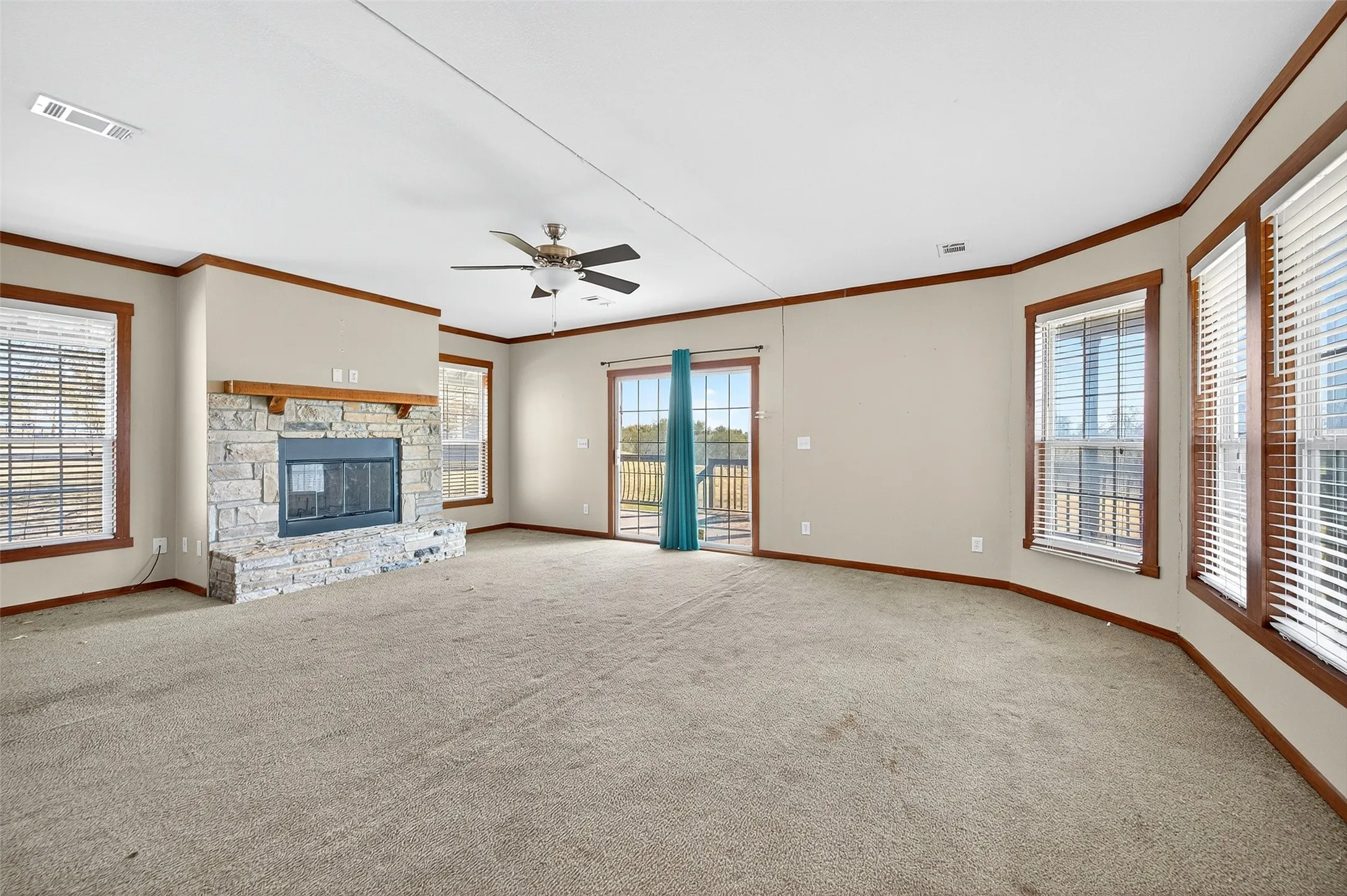 Unfurnished living room with healthy amount of natural light, a stone fireplace, light colored carpet, and crown molding
