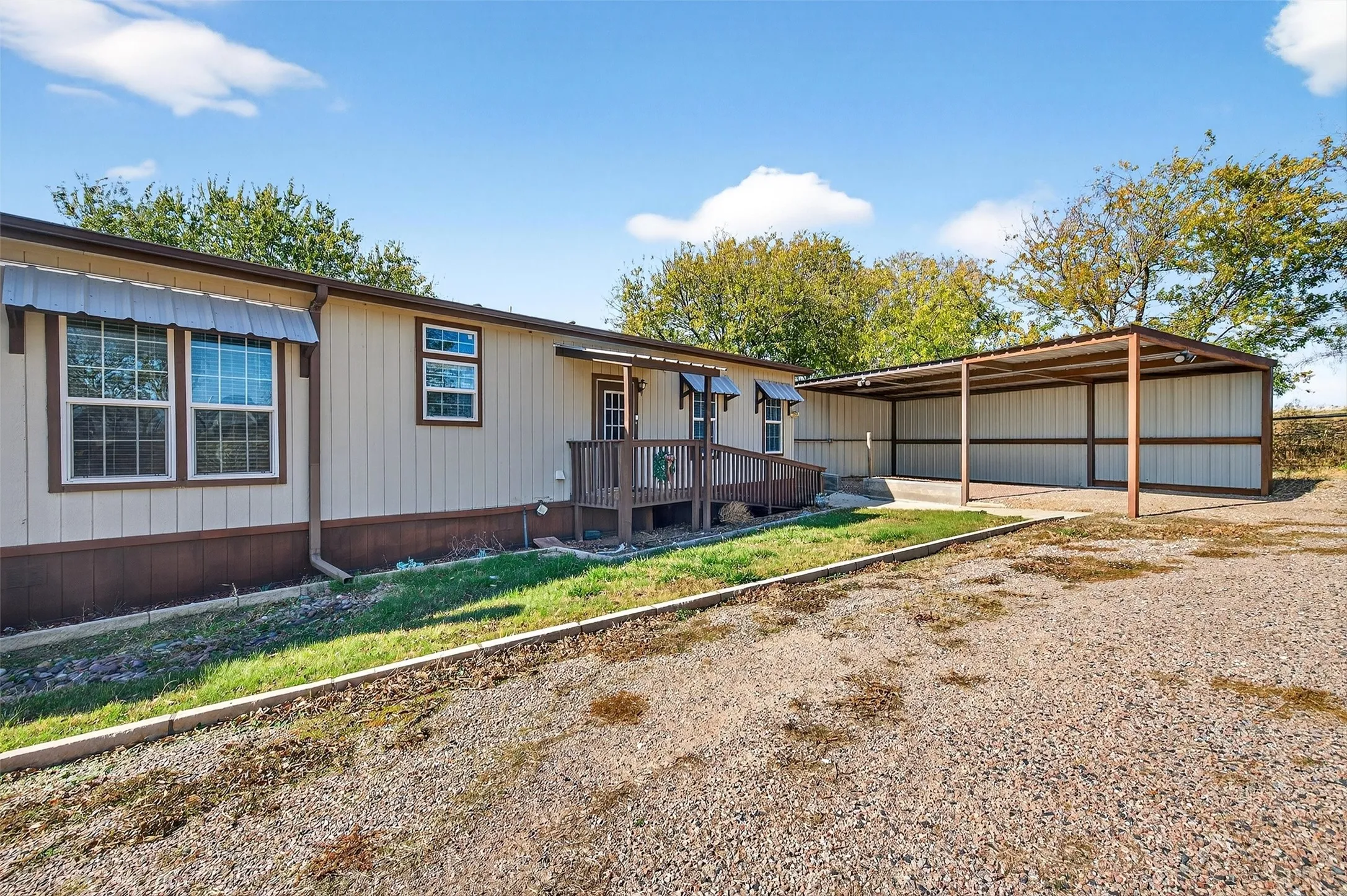View of front of home with a carport, a deck, driveway, and a pole building