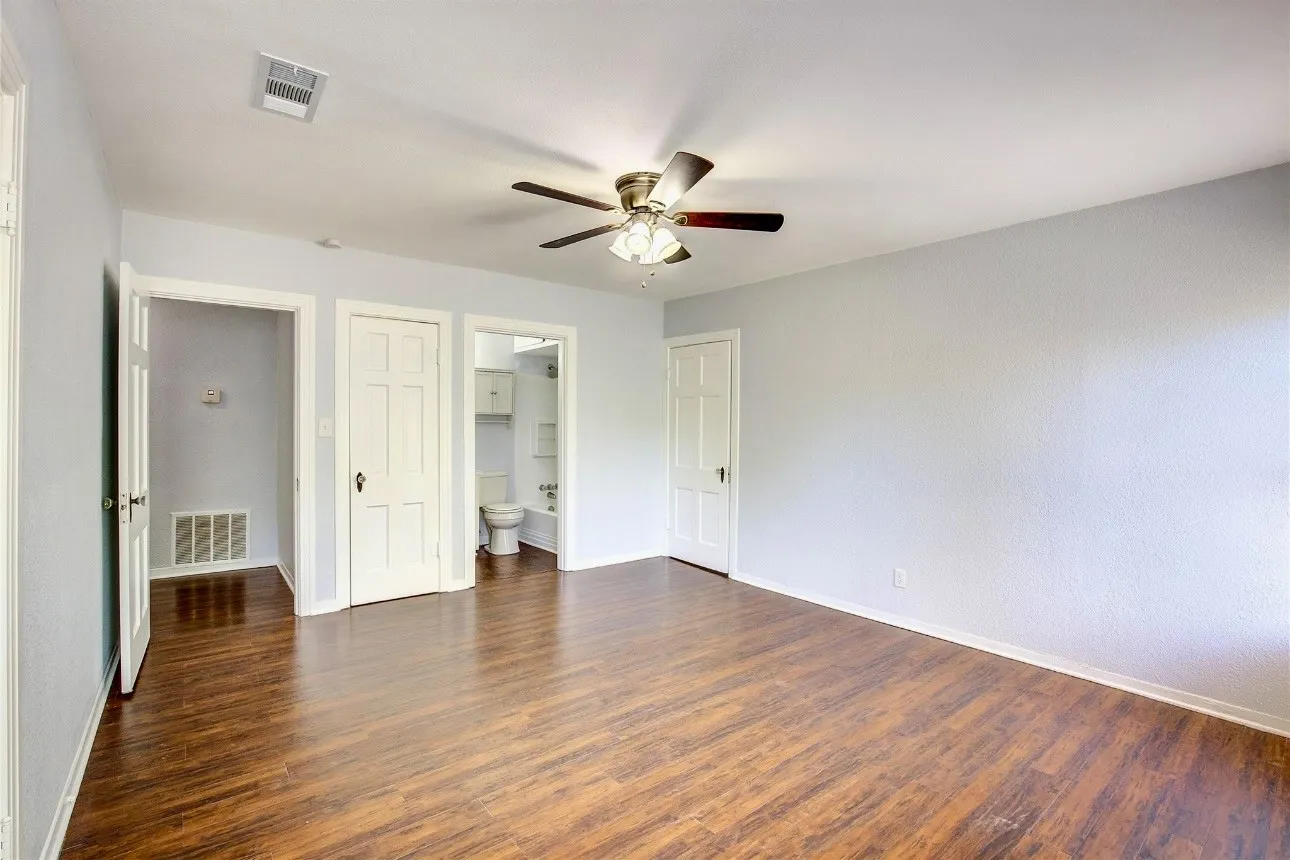 Unfurnished bedroom with ensuite bath, ceiling fan, and dark hardwood / wood-style floors