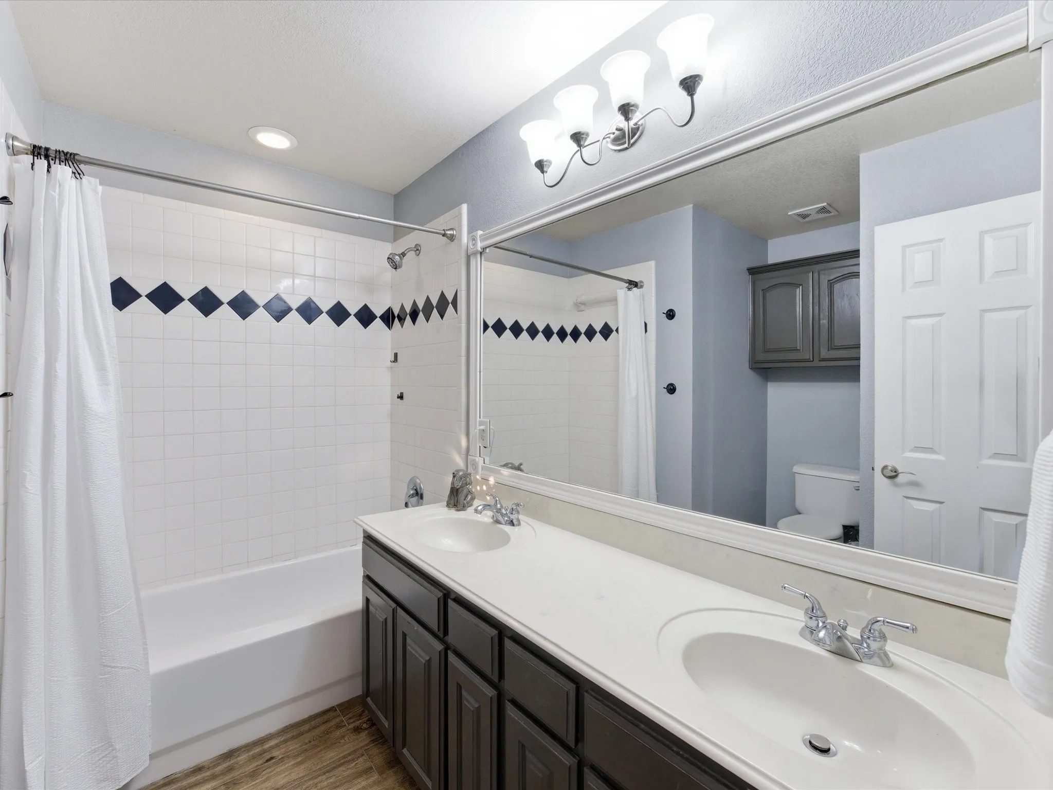 Bathroom with double vanity, shower / bathtub combination with curtain, and dark wood finished floors